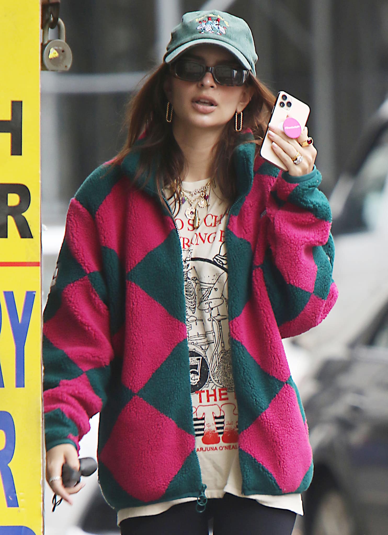 Layered gold necklaces and oversized hoops add a polished edge, while her bold pink-and-green sherpa jacket brings texture and color to an otherwise relaxed, off-duty look
