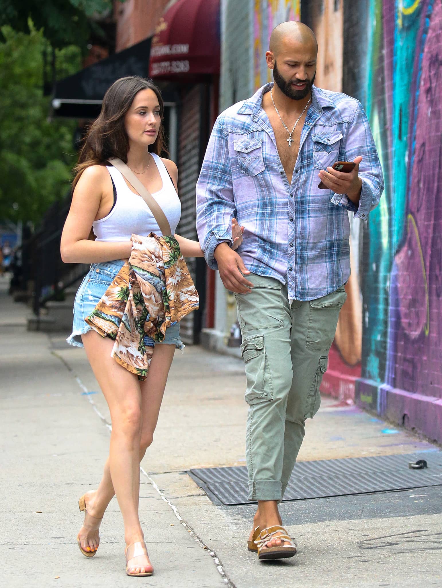 Kacey Musgraves pairs a white tank top and distressed denim shorts with clear-strap Schutz "Victorie" sandals while out with Cole Schafer in New York City