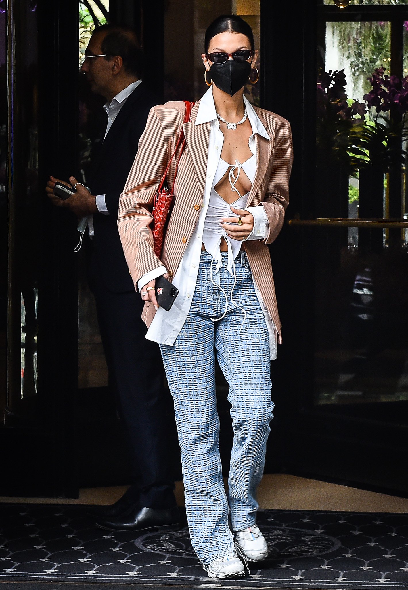 Bella Hadid styled her revealing I.Am.Gia Svana top with layered tailoring, wide-leg Givenchy monogram trousers, and sporty white Salomon sneakers for a sharp mix of Y2K streetwear and Paris Fashion Week off-duty dressing