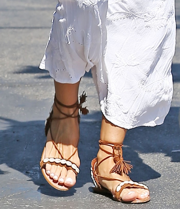 Brown suede lace-up sandals wrap elegantly around the ankle with thin ties and tassel accents, while shell-embellished straps trace the foot for a textured, beachy finish that reinforces the look’s relaxed bohemian feel