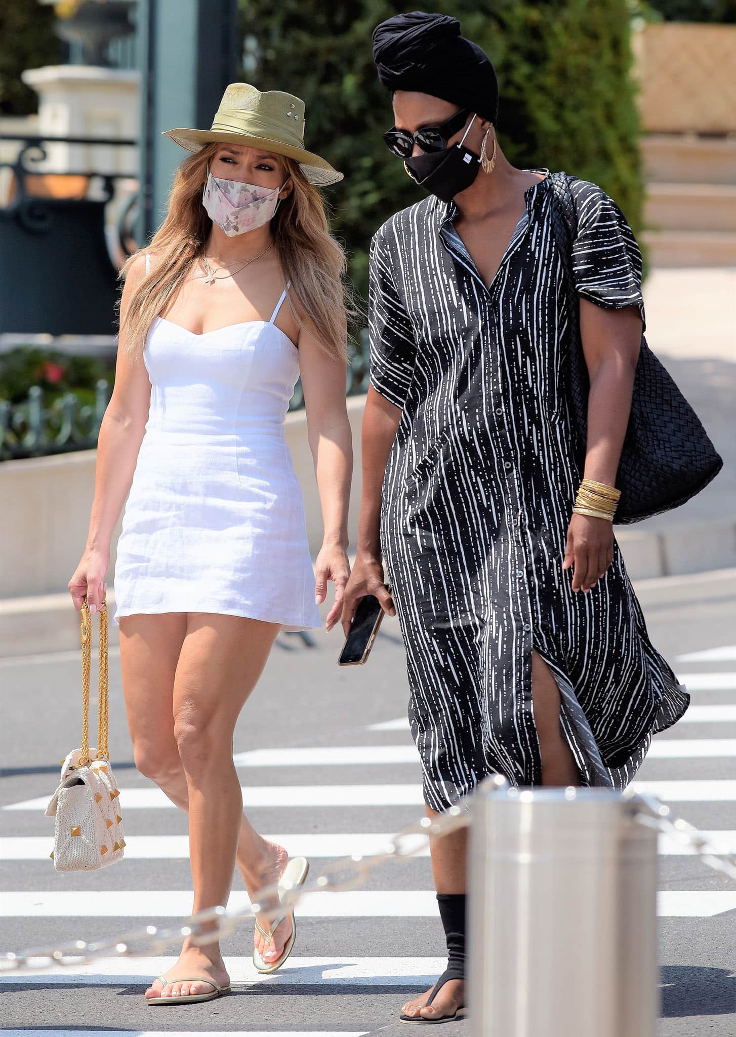 Jennifer Lopez steps out for a stylish shopping trip in Monaco on July 26, 2021, wearing a white Reformation mini dress, gold flip-flops, a floral face mask, and a Valentino Roman Stud crochet bag