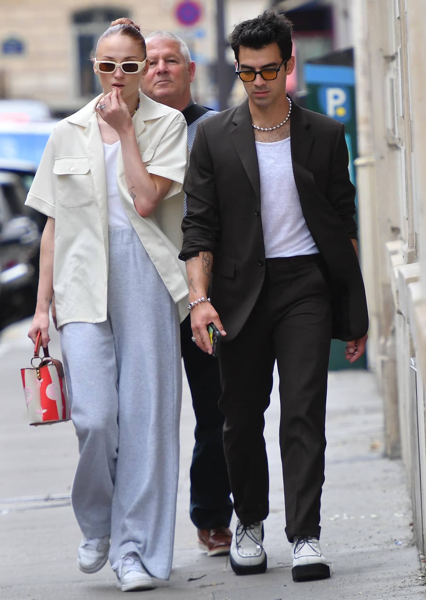 Sophie Turner keeps it effortlessly cool in Nike Dunk Low “Photon Dust” sneakers and relaxed gray sweats while Joe Jonas sharpens his dark brown tailoring with white platform brogues as they step out during Paris Fashion Week