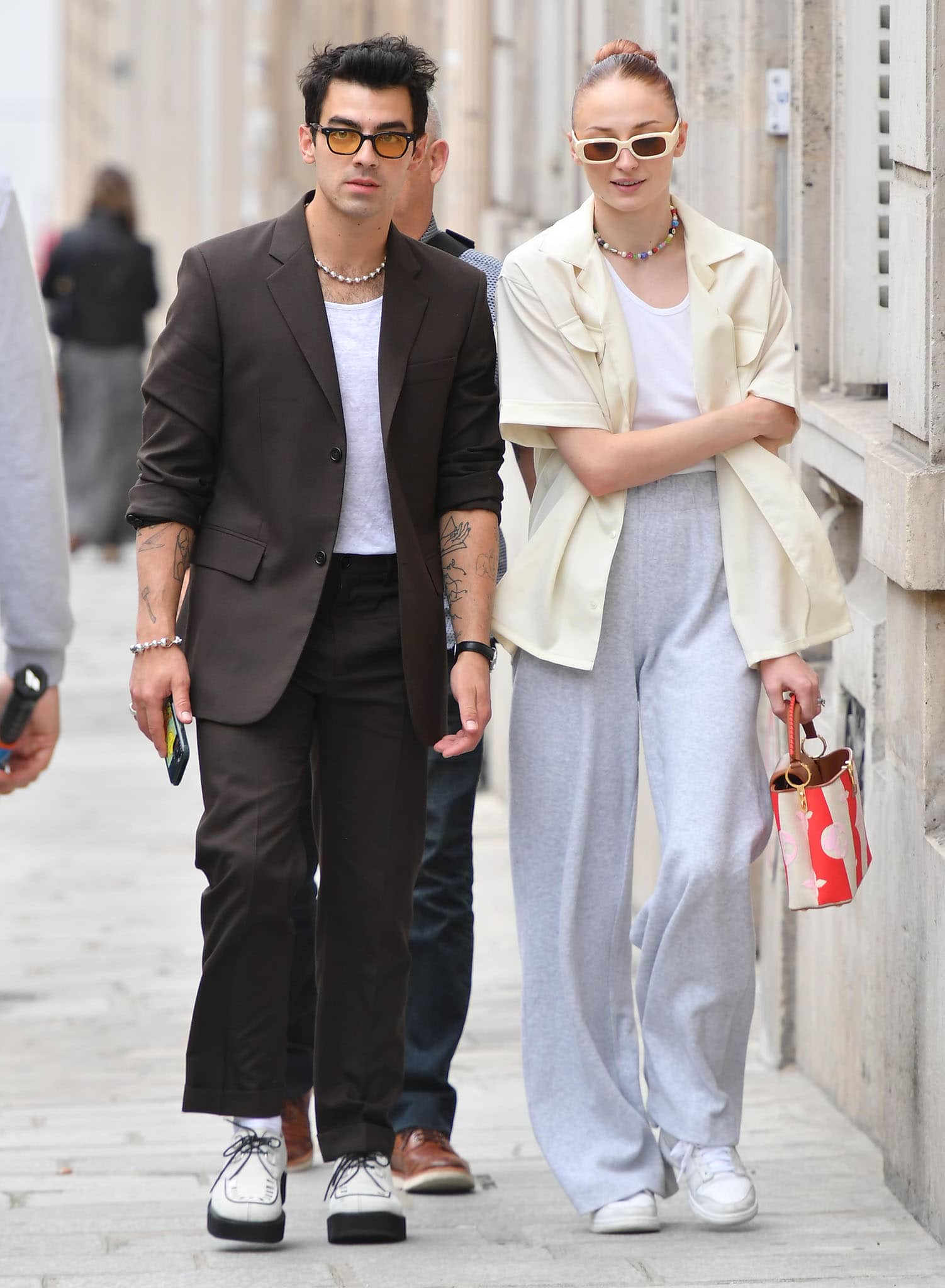 Joe Jonas sharpens his relaxed brown tailoring with a crisp white tee, chunky white platform brogues, and amber-tinted sunglasses, adding retro edge to his Paris Fashion Week street look