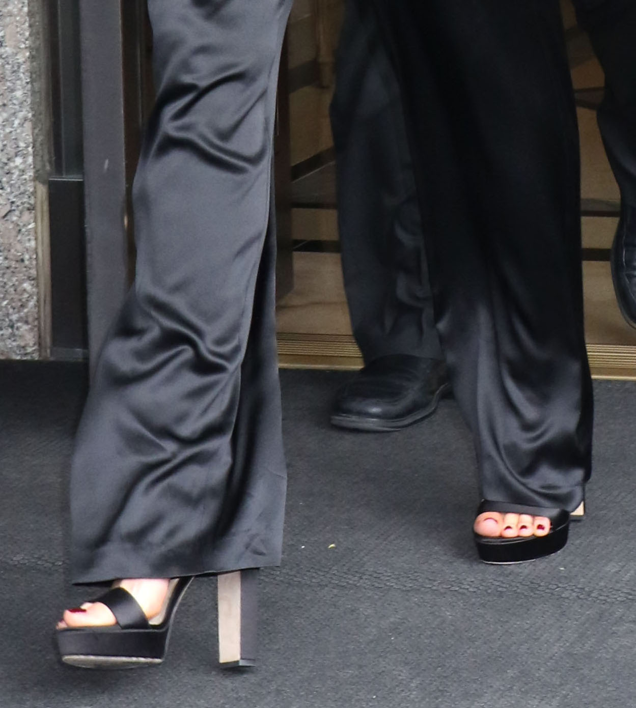 Kate Beckinsale shows off a dark burgundy pedicure in Jimmy Choo’s “Holly” platform sandals, using the towering block heels and chunky platforms to add striking height and balance to her sleek all-black satin separates