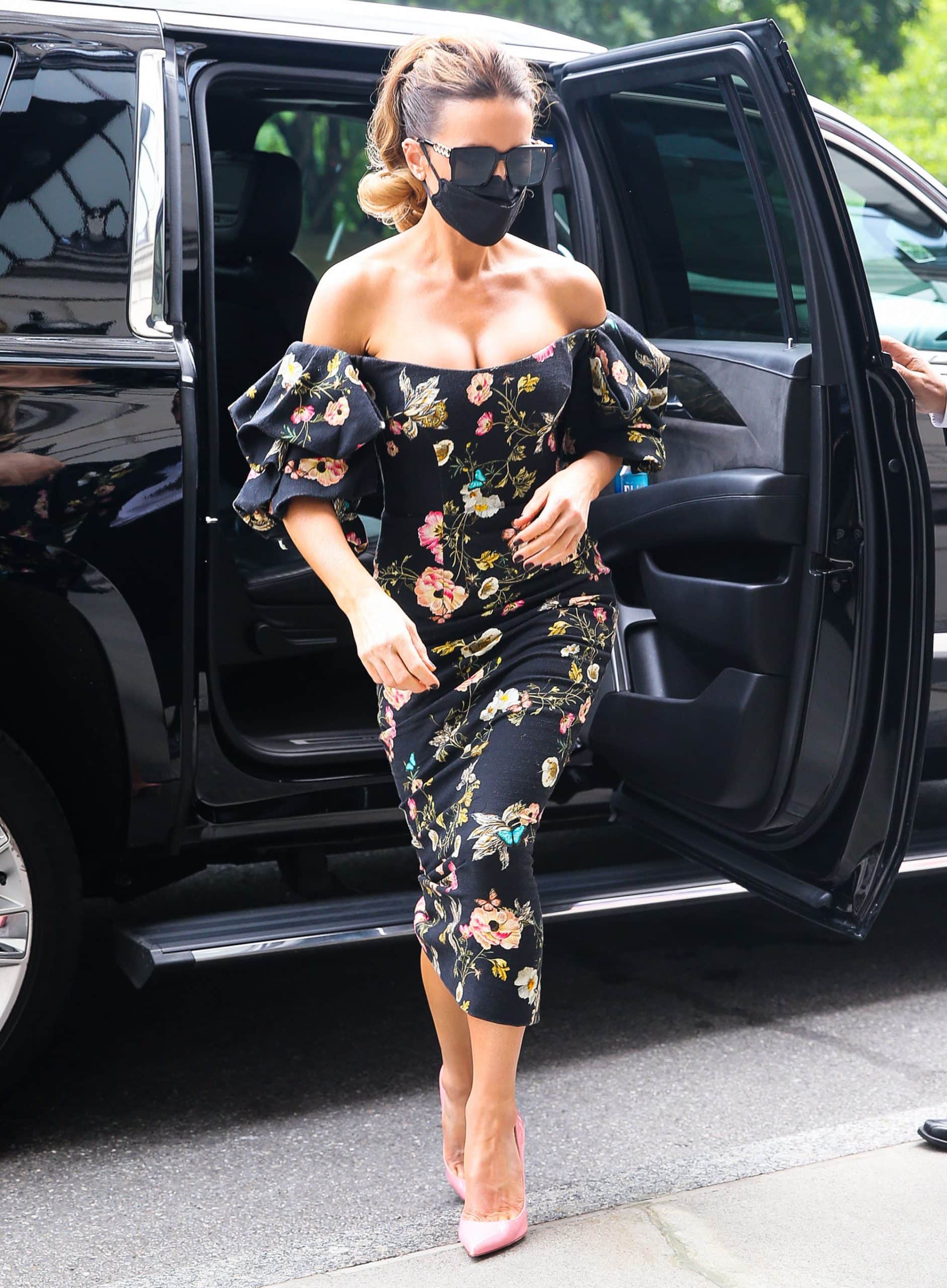 Kate Beckinsale embraces romantic glamour in a floral Monique Lhuillier midi dress with dramatic puffed sleeves and an off-the-shoulder neckline, completing the look with bubblegum-pink Christian Louboutin pumps that bring a playful pop of color to the dark botanical print