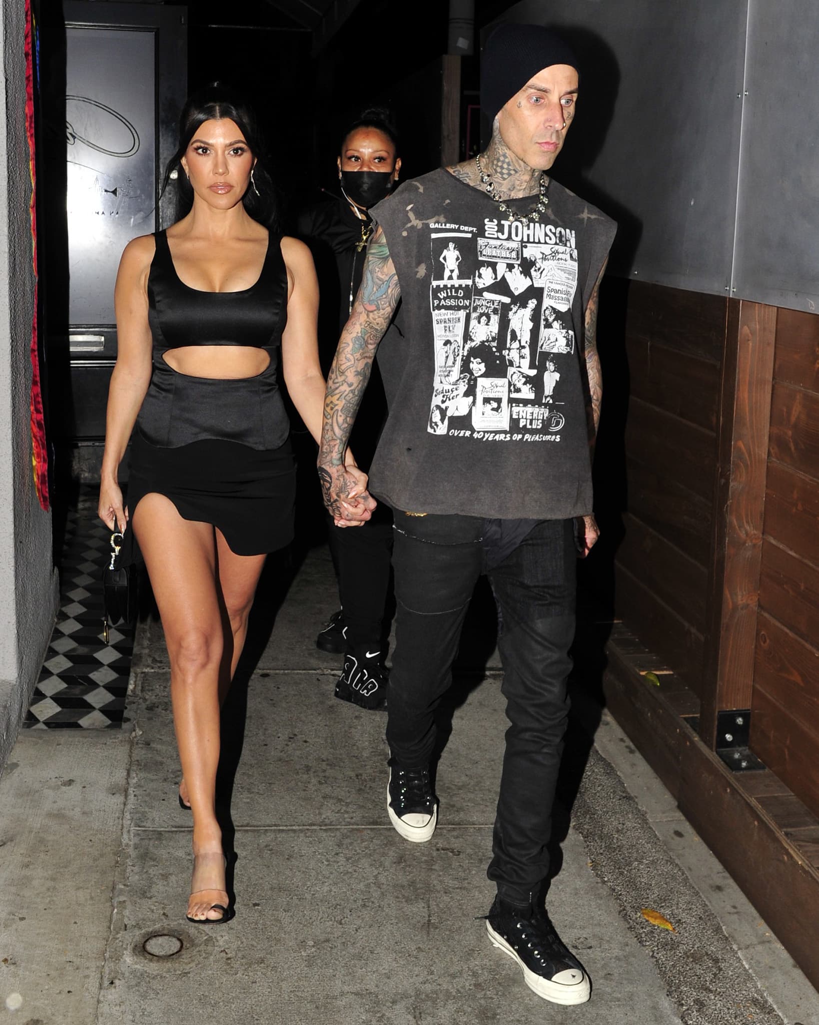 Hand in hand, Kourtney Kardashian contrasted Travis Barker's grunge-inspired style with a sculptural cutout outfit finished by transparent PVC heels and a vintage Dior Saddle Bag