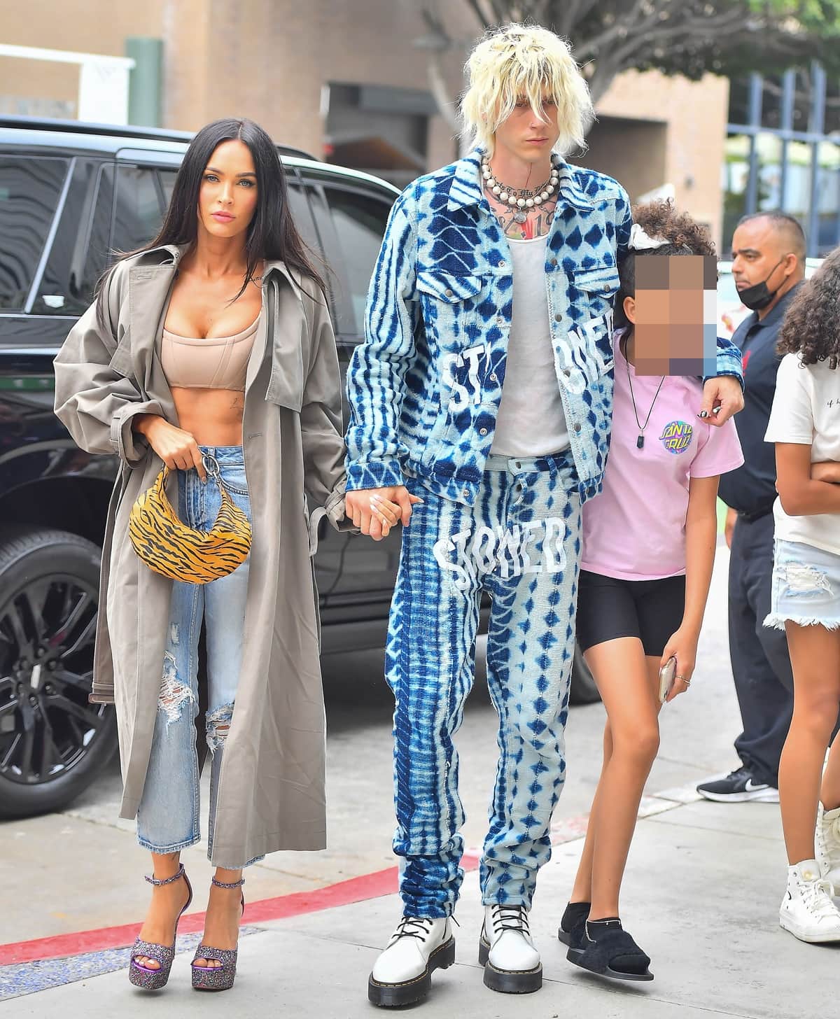 Megan Fox balances an oversized Acne Studios trench with a sculpted Alexander Wang corset bra, distressed Ksubi jeans, and glittering Amina Muaddi platform sandals, punctuated by a tiger-print By Far bag, during a June 19, 2021 outing in Santa Monica