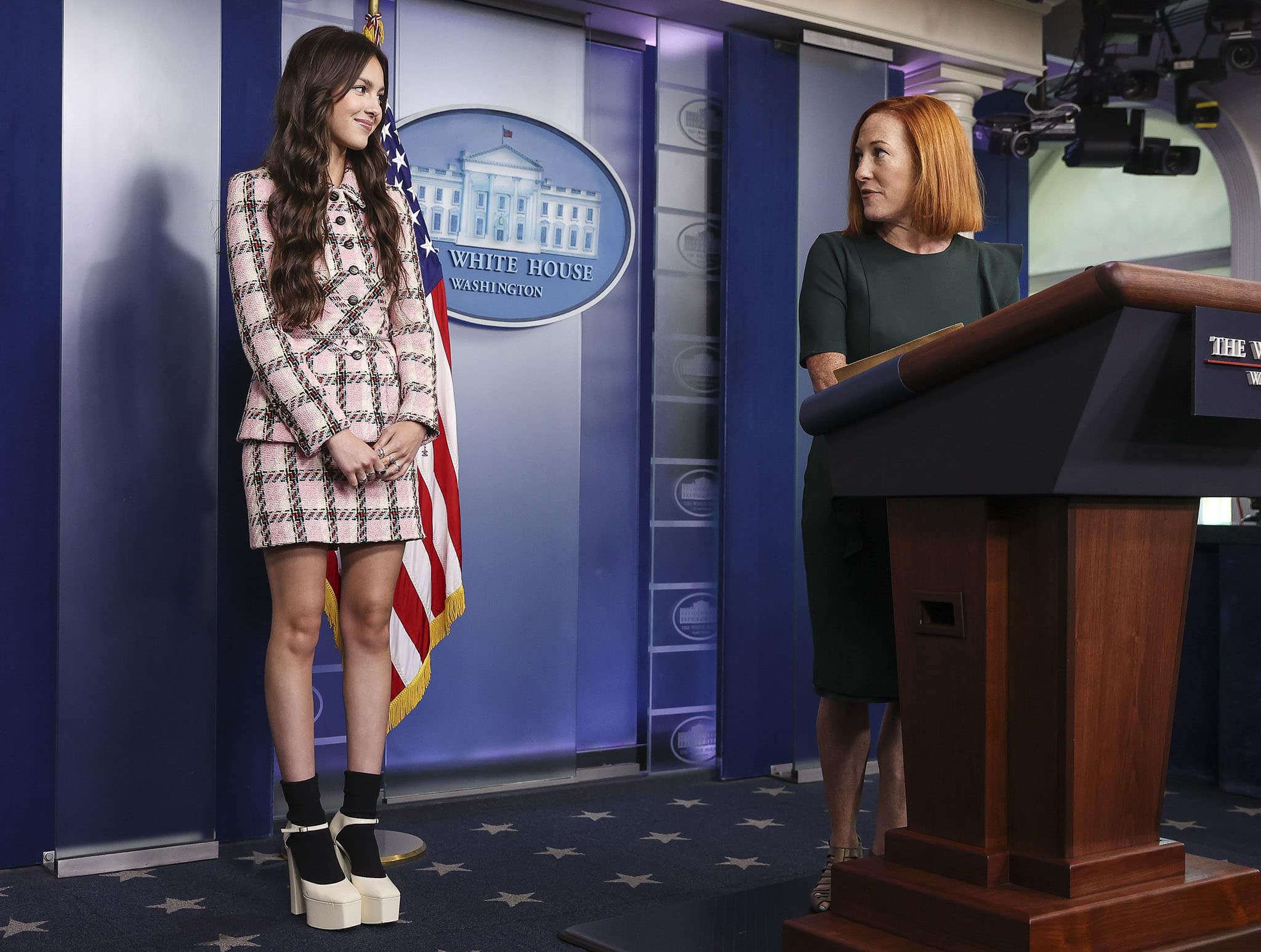 Olivia Rodrigo joins the White House press briefing in Washington, D.C., in July 2021, wearing a pink plaid Chanel tweed set styled with towering white platform Mary Jane heels and black ankle socks, a polished yet playful look that blends vintage tailoring with Gen-Z edge