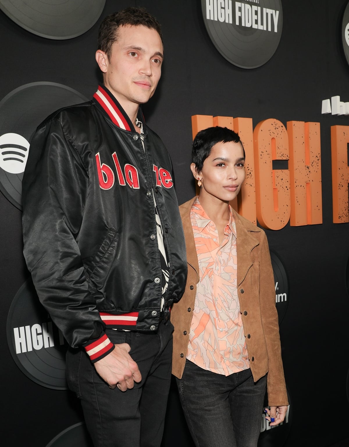 Zoë Kravitz and Karl Glusman attend the 'High Fidelity' premiere, with Zoë rocking a soft retro look in a floral button-down, suede jacket, and high-waisted jeans, while Karl keeps it casual in a varsity-style satin bomber and dark denim