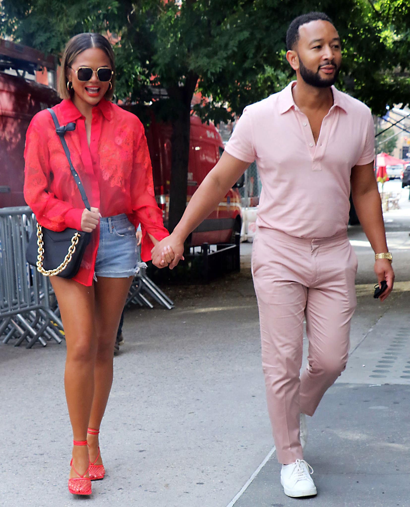 Chrissy Teigen showcases her toned legs in red wraparound mesh pumps and cutoff denim shorts while strolling hand-in-hand with John Legend through Soho in New York City on August 20, 2021
