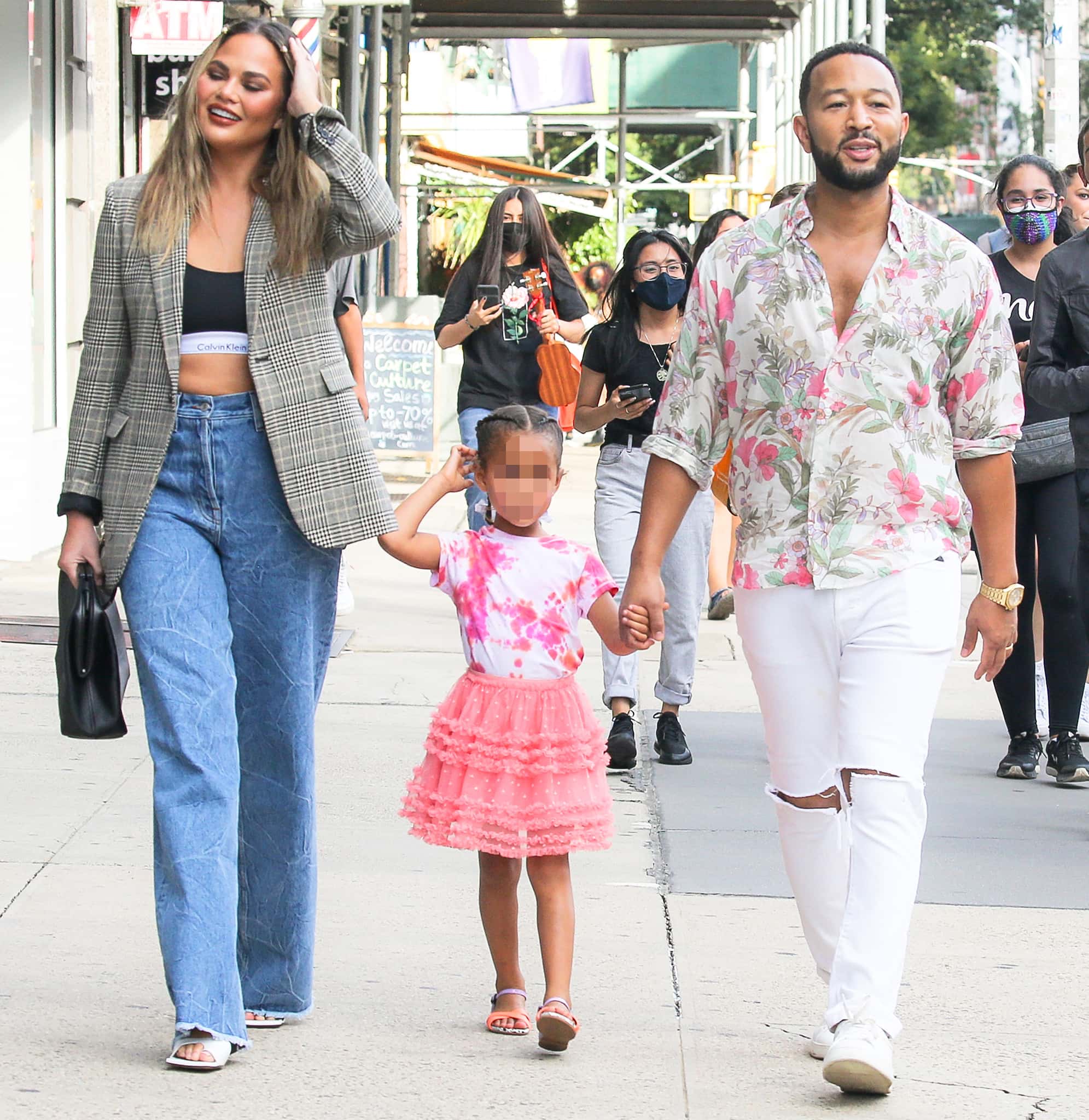 Chrissy Teigen channels ’90s minimalism in a plaid blazer, Calvin Klein sports bra, wide-leg jeans, and white square-toe mules as she strolls hand-in-hand with John Legend and daughter Luna in New York City on August 19, 2021