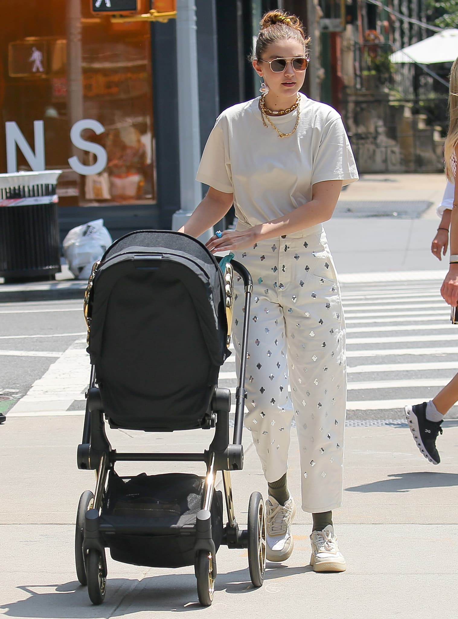 Gigi Hadid crosses a Manhattan street with Khai, pairing embellished white jeans with Reebok x Victoria Beckham Dual Court sneakers for a practical take on summer street style