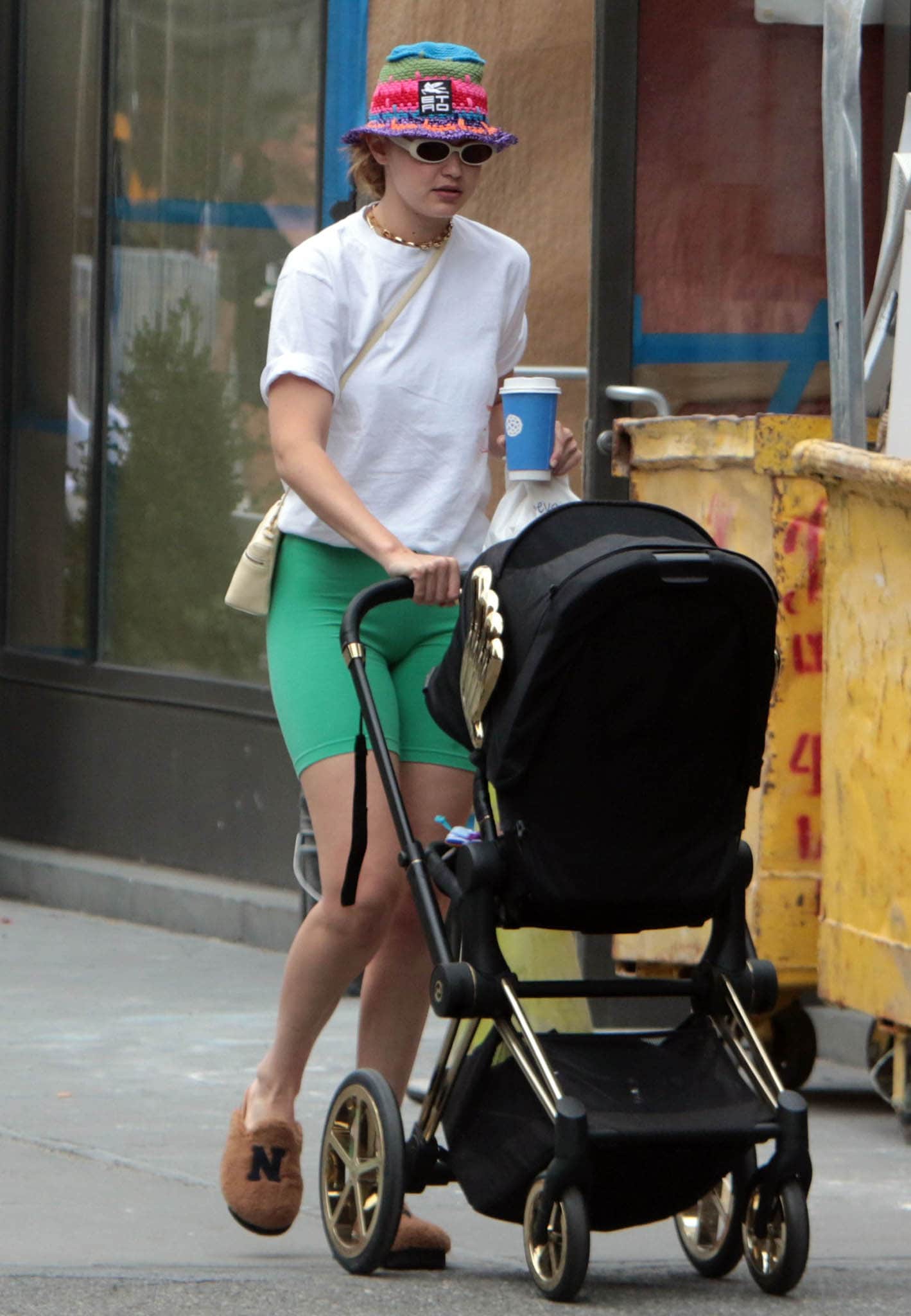 Gigi Hadid pushes Khai through New York City in a white tee, green biker shorts, and fuzzy Joshua Sanders NY mules that emphasize comfort over runway polish
