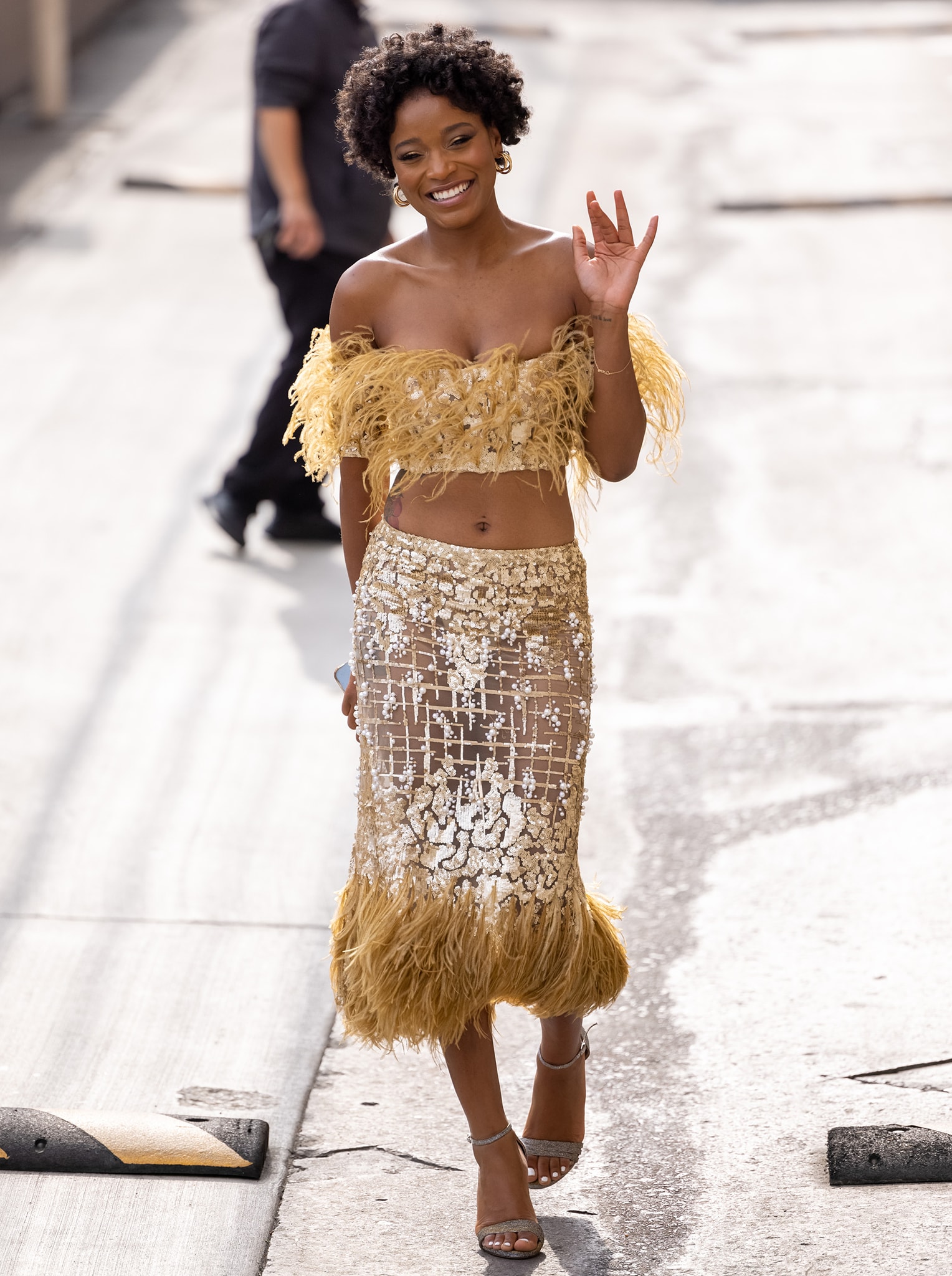 Keke Palmer steps out in a gilded Georges Chakra feather-and-sequin ensemble, finishing the look with sparkling silver Sarah Flint “Perfect” sandals that show off her white pedicure