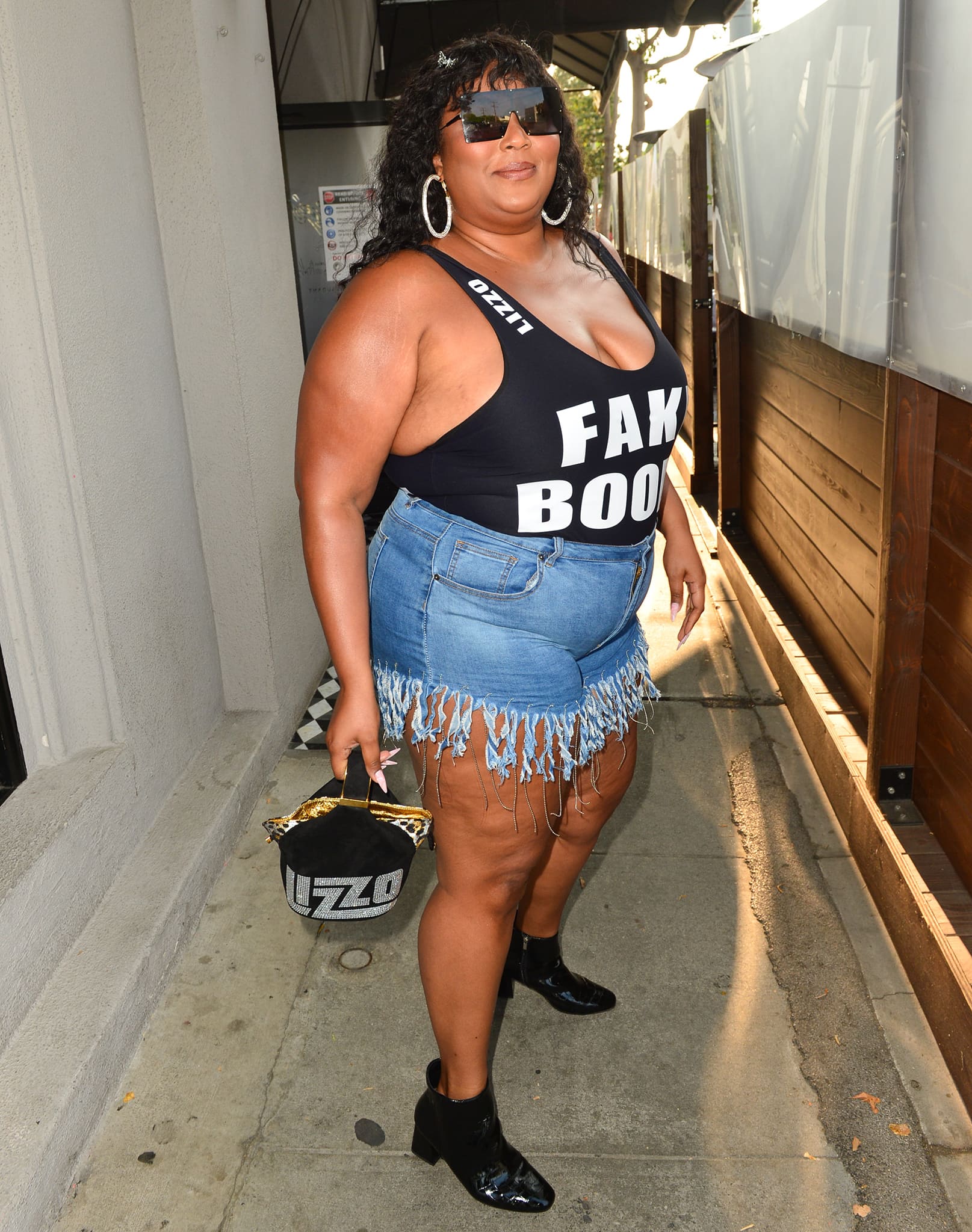 Lizzo accessorizes with oversized square sunglasses, crystal hoop earrings, and a custom rhinestone bucket bag bearing her name while stepping out in Los Angeles