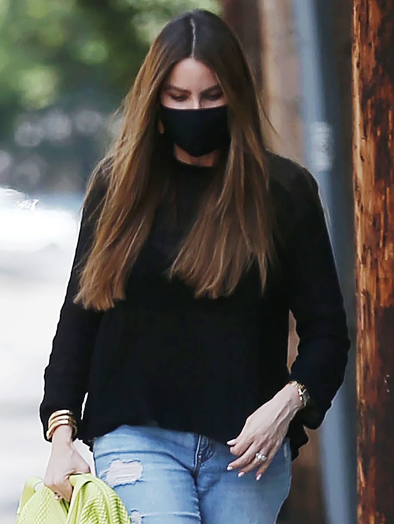 Sofia Vergara wears straight brown hair, hoop earrings, eyeliner, smoky eye makeup, and a black face mask
