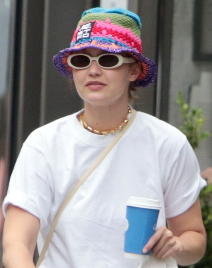 Oval sunglasses, a shell necklace, and a vibrant crochet bucket hat add playful contrast to Gigi Hadid's relaxed off-duty ensemble