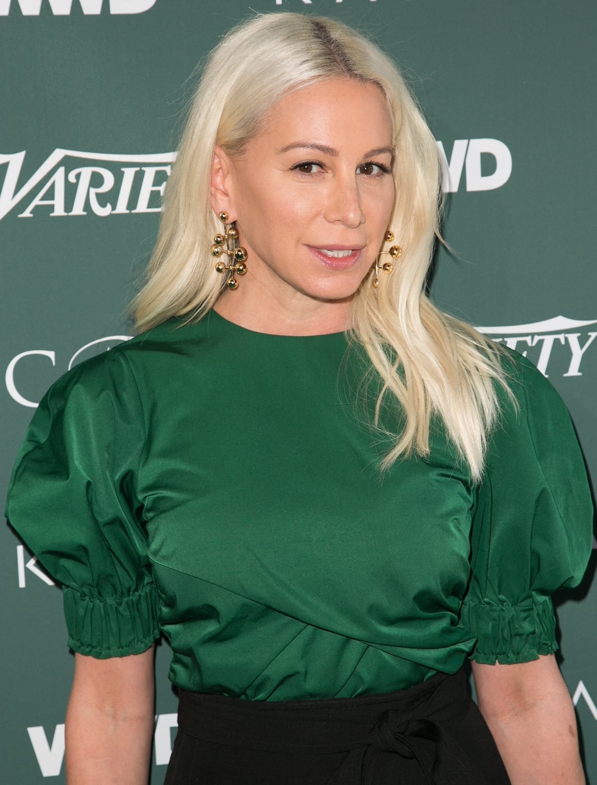 Jennifer Fisher exudes effortless sophistication in statement gold earrings from her eponymous jewelry line, perfectly complementing her chic emerald green ensemble