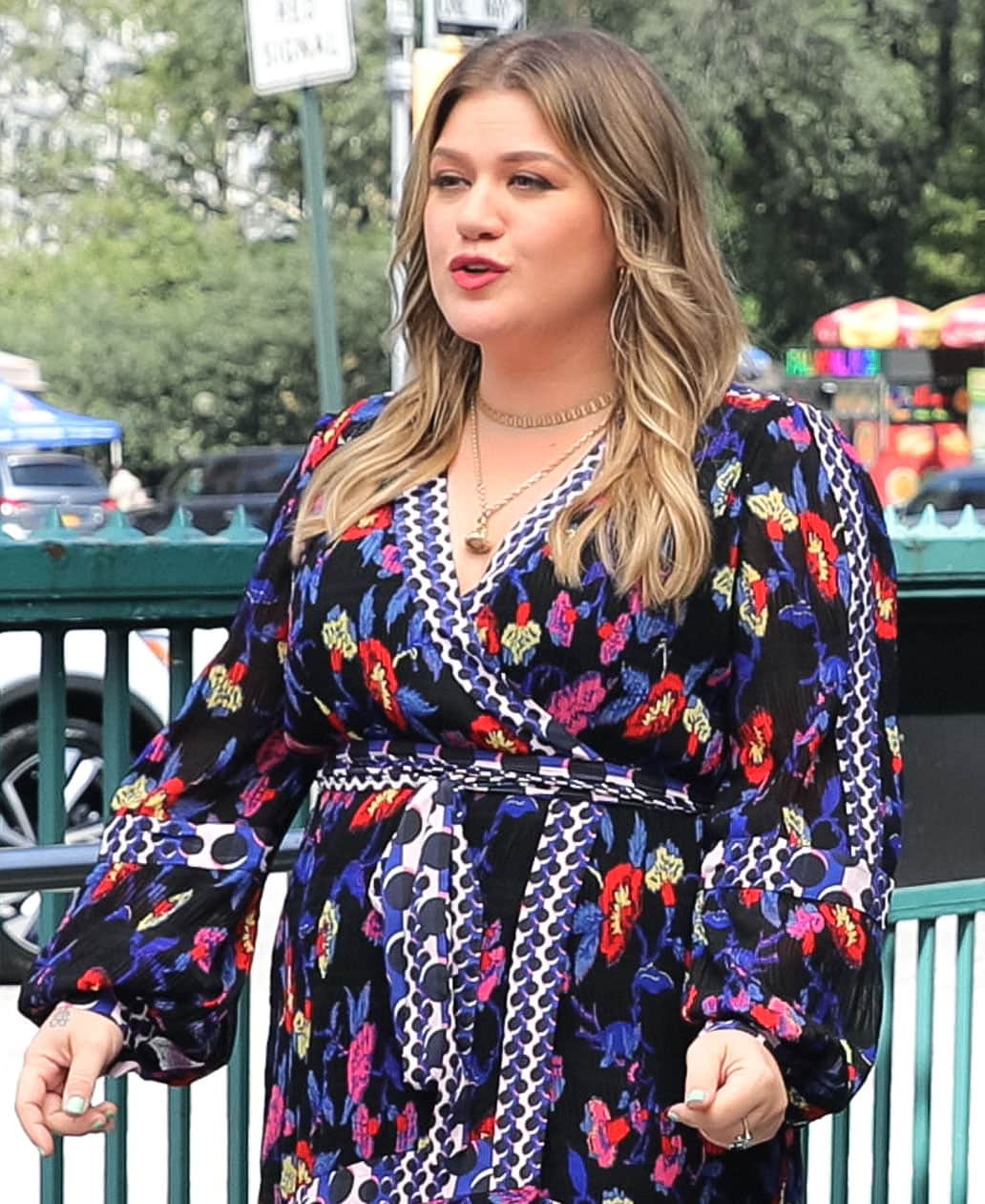 Kelly Clarkson complements her floral Diane von Furstenberg wrap dress with softly feathered waves, layered gold jewelry, and a bold red lip during a promotional shoot in New York City