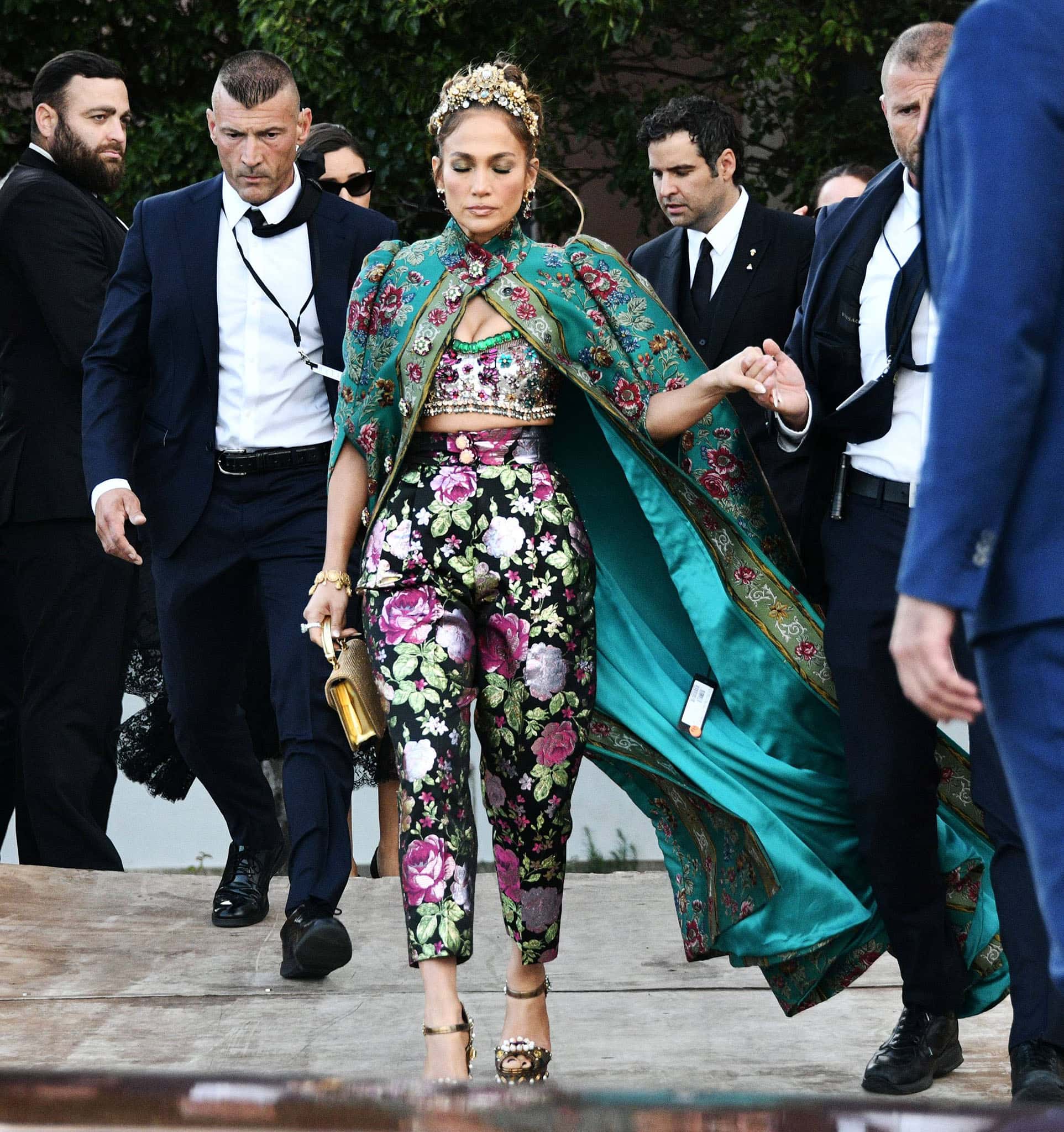 Jennifer Lopez channels full Alta Moda extravagance in a crystal-embellished Dolce Gabbana bralette, floral jacquard trousers, and jeweled Keira platform sandals beneath a sweeping turquoise cape in Venice