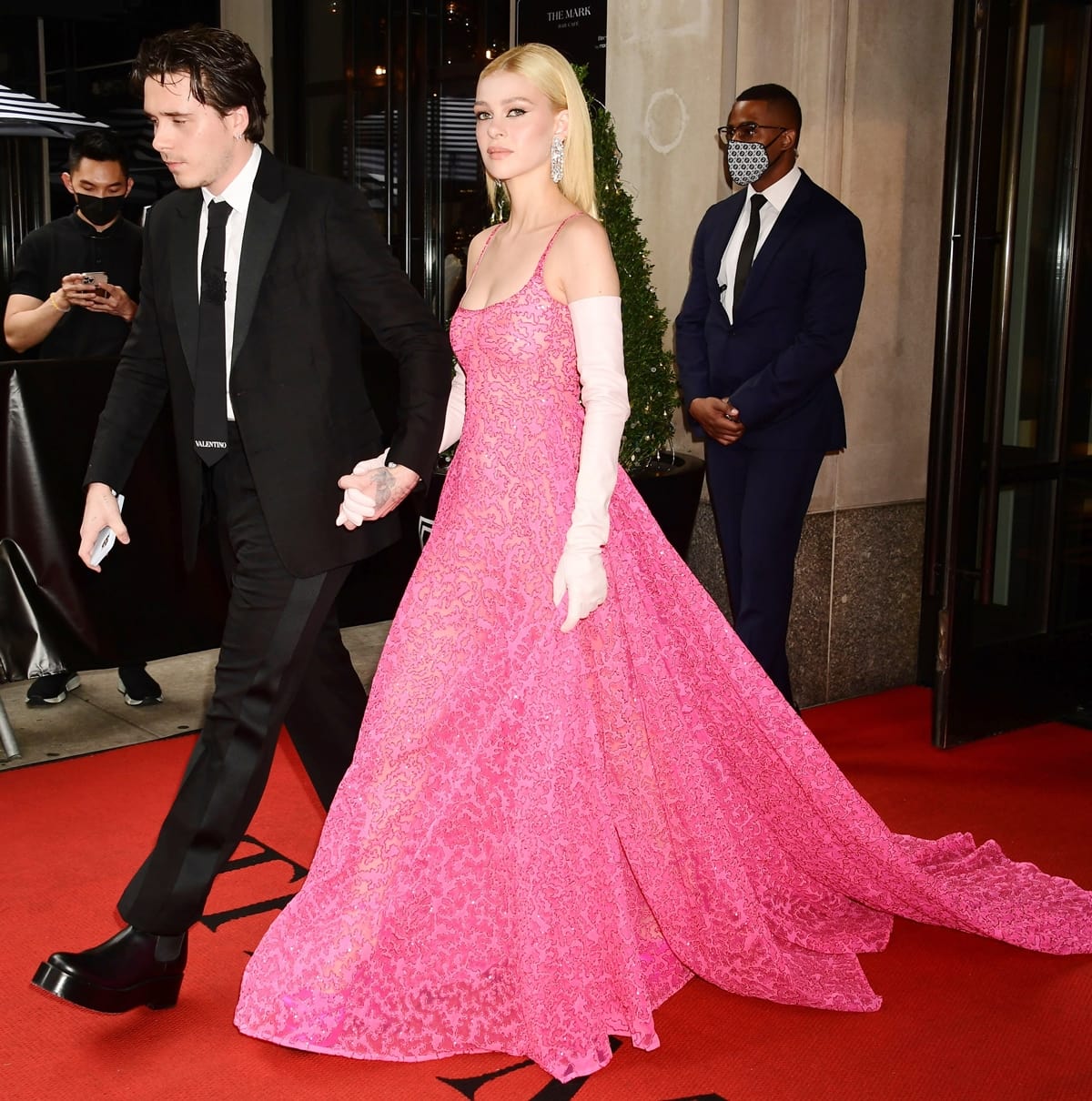 Brooklyn Beckham and Nicola Peltz arrive at the 2021 Met Gala in coordinated Valentino looks, with Nicola wearing a sparkling pink couture gown, opera gloves, and hidden Versace Medusa Aevitas platform pumps