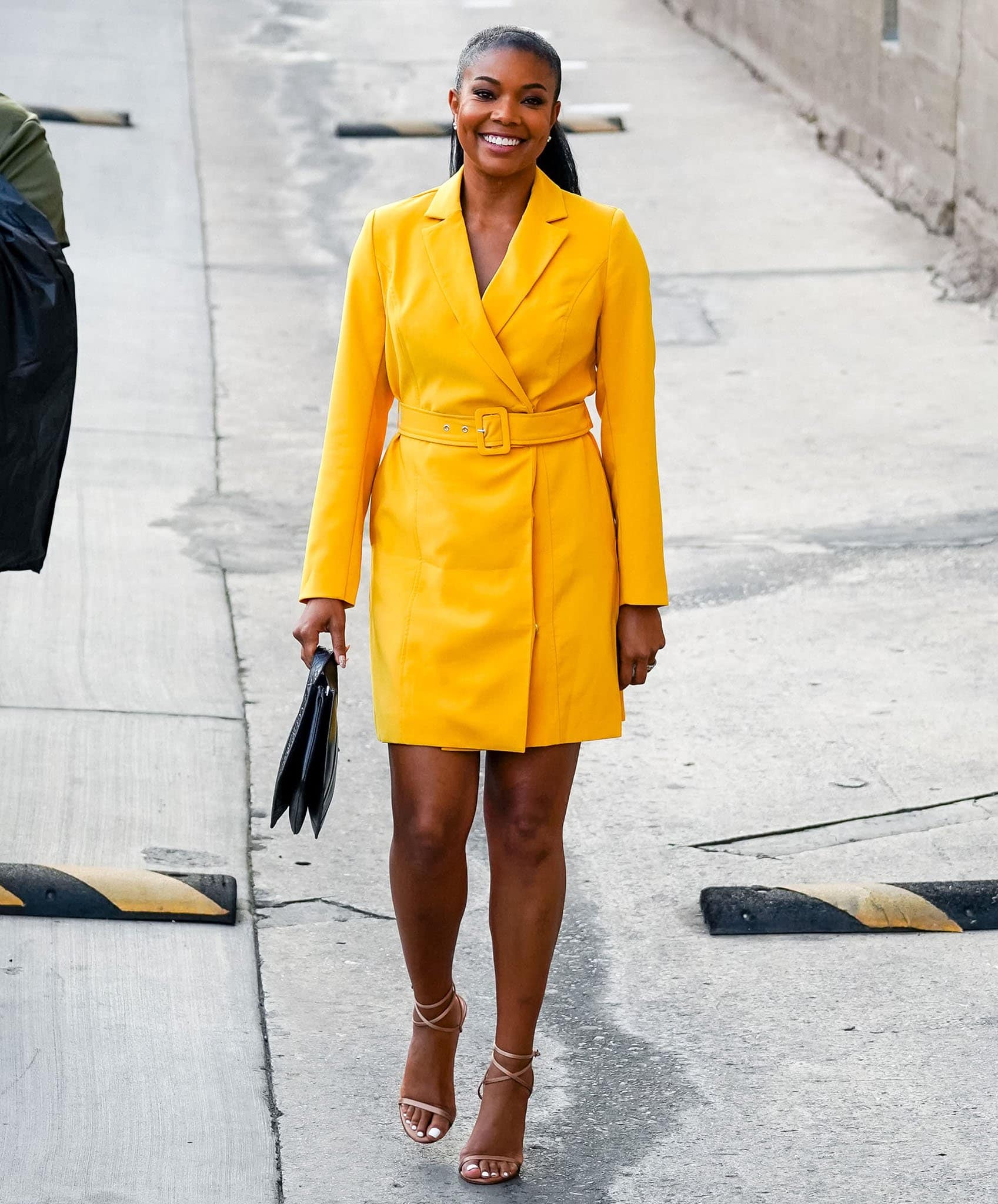 Gabrielle Union brightens the streets in a sunshine-yellow wrap coat dress, pairing the bold look with strappy nude sandals and a sleek ponytail outside the Jimmy Kimmel Live studio on September 28, 2021