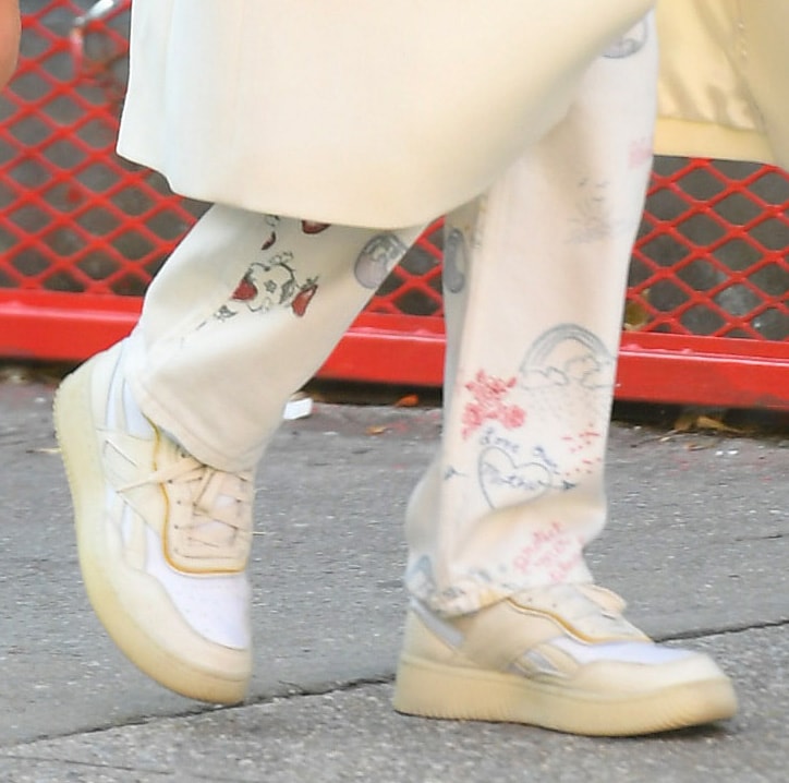 Gigi Hadid grounds her layered fall outfit with Reebok x Victoria Beckham Dual Court II trainers, pairing the cream-toned sneakers with doodle-print Reformation trousers for a relaxed take on retro-inspired street style