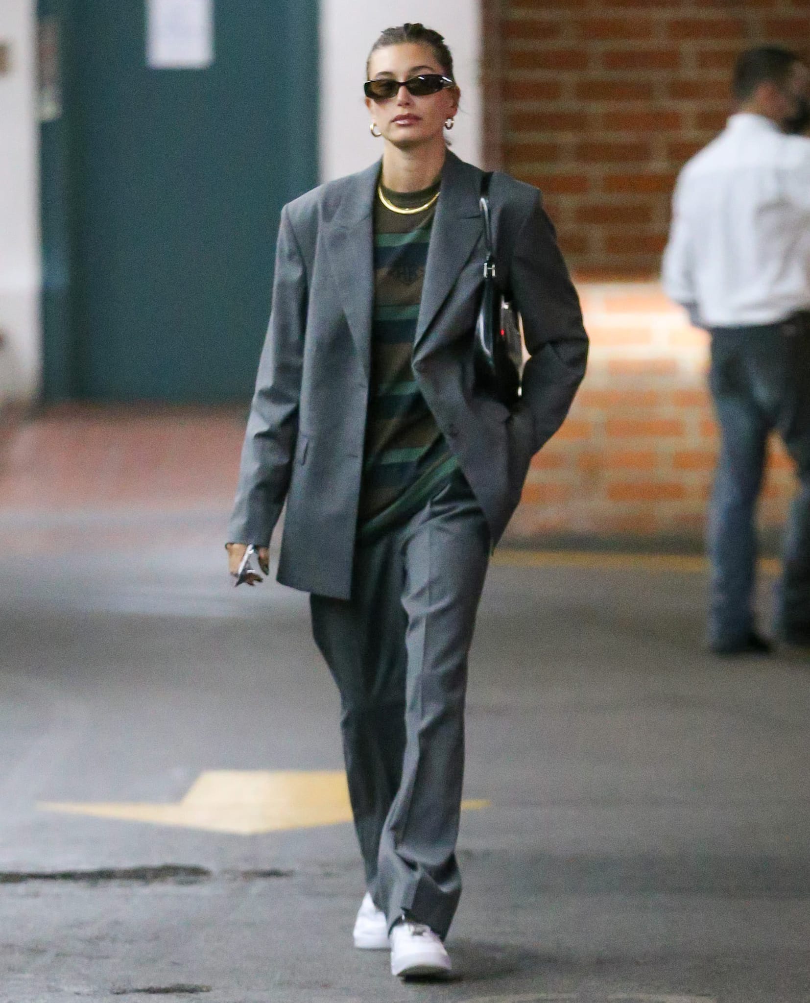 Hailey Bieber elevated an oversized Han Kjøbenhavn gray suit with crisp white Nike Air Force 1 sneakers, proving that classic basketball shoes remain the foundation of her effortlessly androgynous street style on October 19, 2021