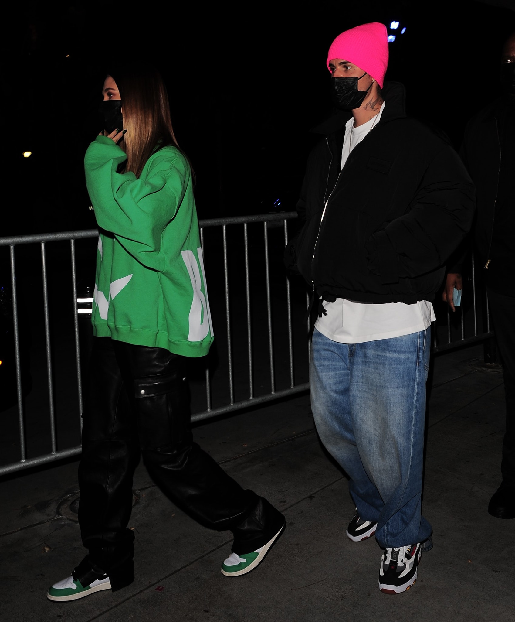 Justin Bieber added a pop of color to his relaxed Lakers game look with a neon-pink beanie, oversized black bomber jacket, baggy jeans, and chunky retro sneakers, while Hailey Bieber coordinated her green Ghost sweatshirt with black leather trousers and Lucky Green Air Jordan 1 High OG sneakers