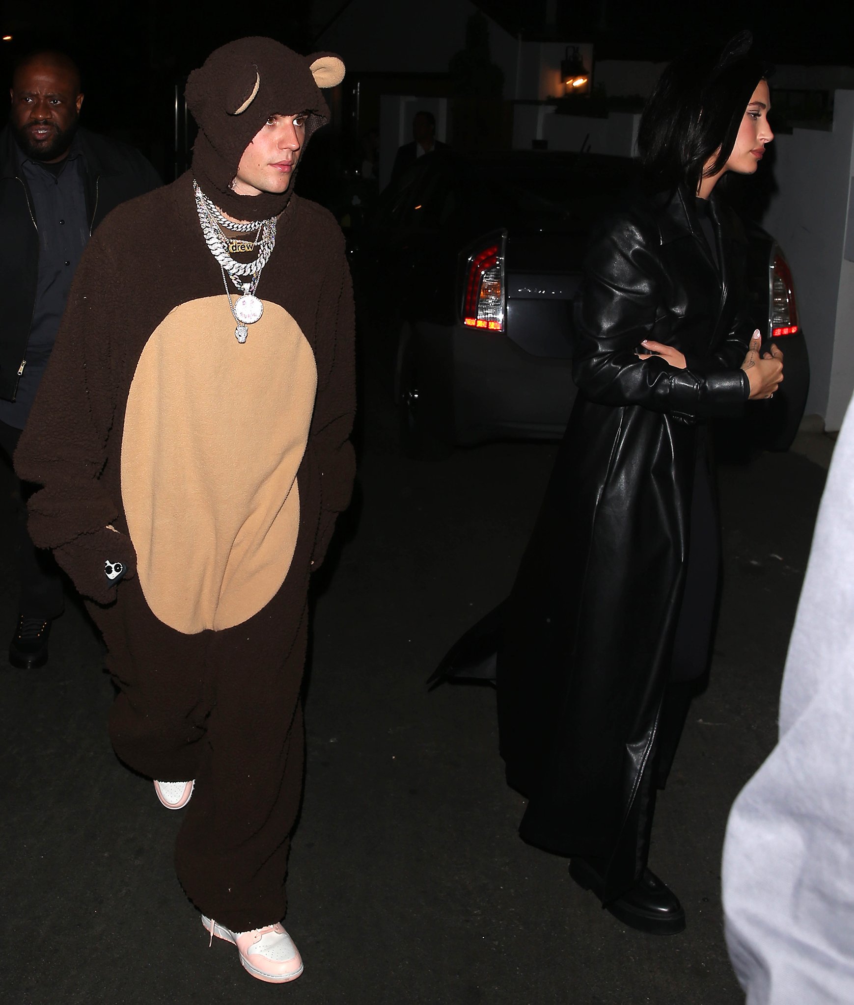 Justin Bieber embraced playful Halloween dressing in a plush brown bear costume and white-and-pink sneakers, while Hailey Bieber sharpened the contrast beside him in a sweeping black leather trench layered over her Catwoman look and chunky-soled The Row ankle boots