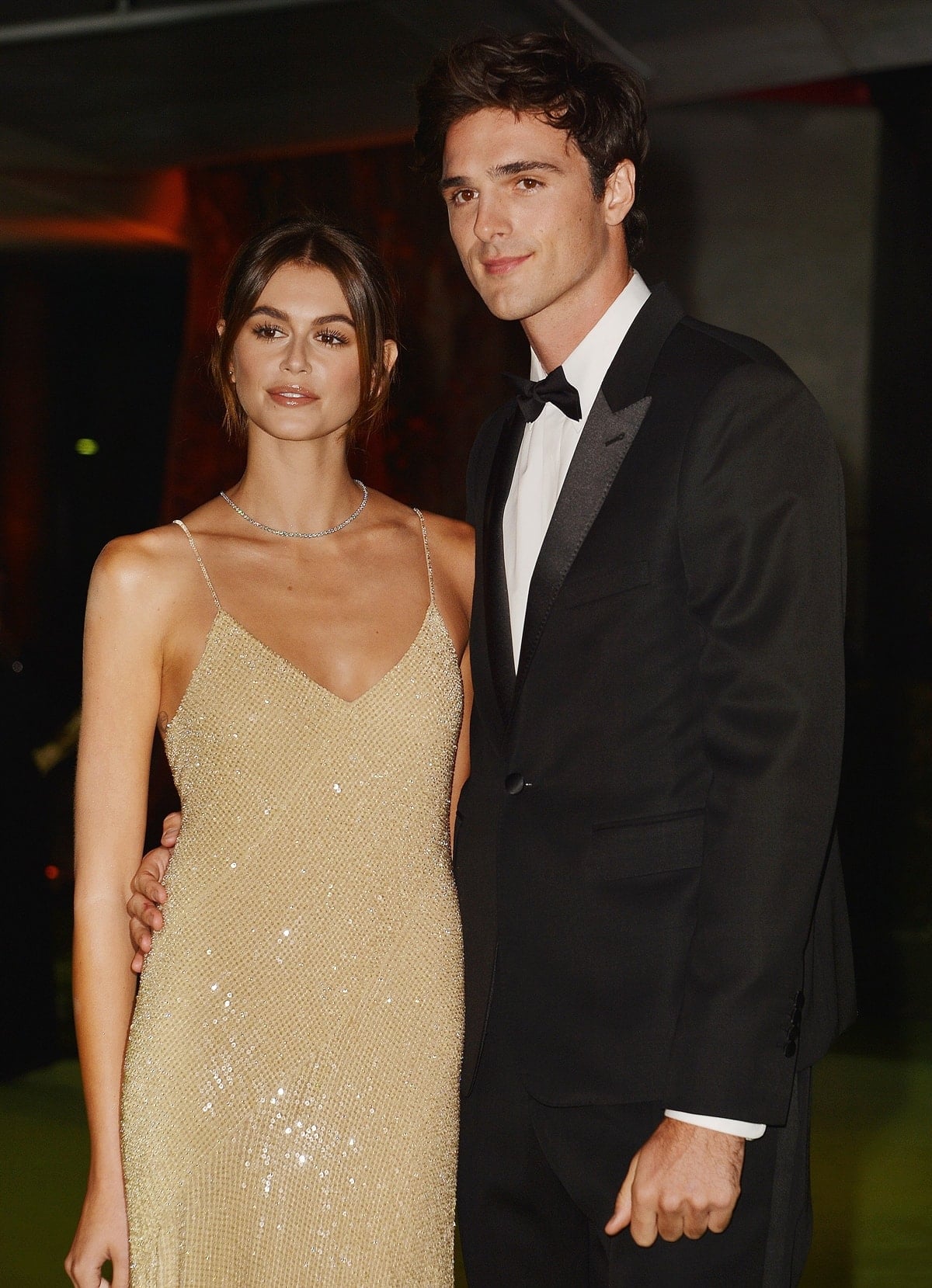 Kaia Gerber stuns in a shimmering gold slip dress while posing with Jacob Elordi, who looks sharp in a classic black tuxedo