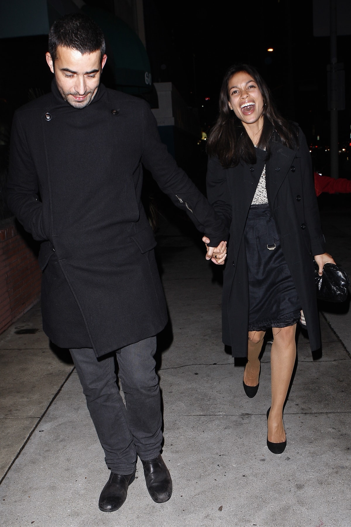 Rosario Dawson leaves La Vida restaurant hand-in-hand with then-boyfriend Mathieu Schreyer, looking chic in a black coat, satin skirt, and classic black pumps after attending Quentin Tarantino’s party in Hollywood on February 9, 2010