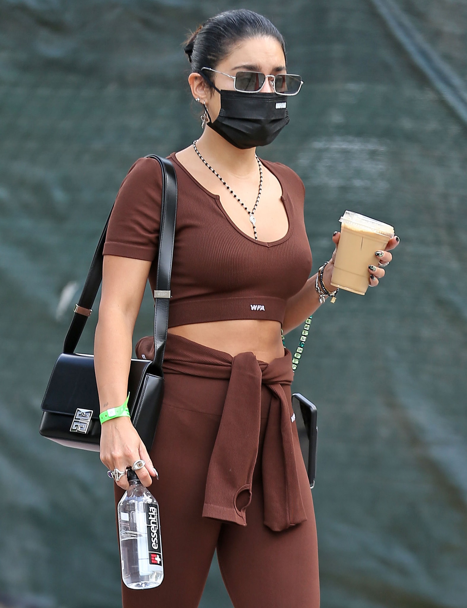 Vanessa Hudgens keeps her gym-run style sleek and unfussy, pairing a chocolate-brown White Fox crop top and leggings with layered silver jewelry, a Givenchy 4G crossbody bag, and an iced coffee in hand as she steps out post-workout
