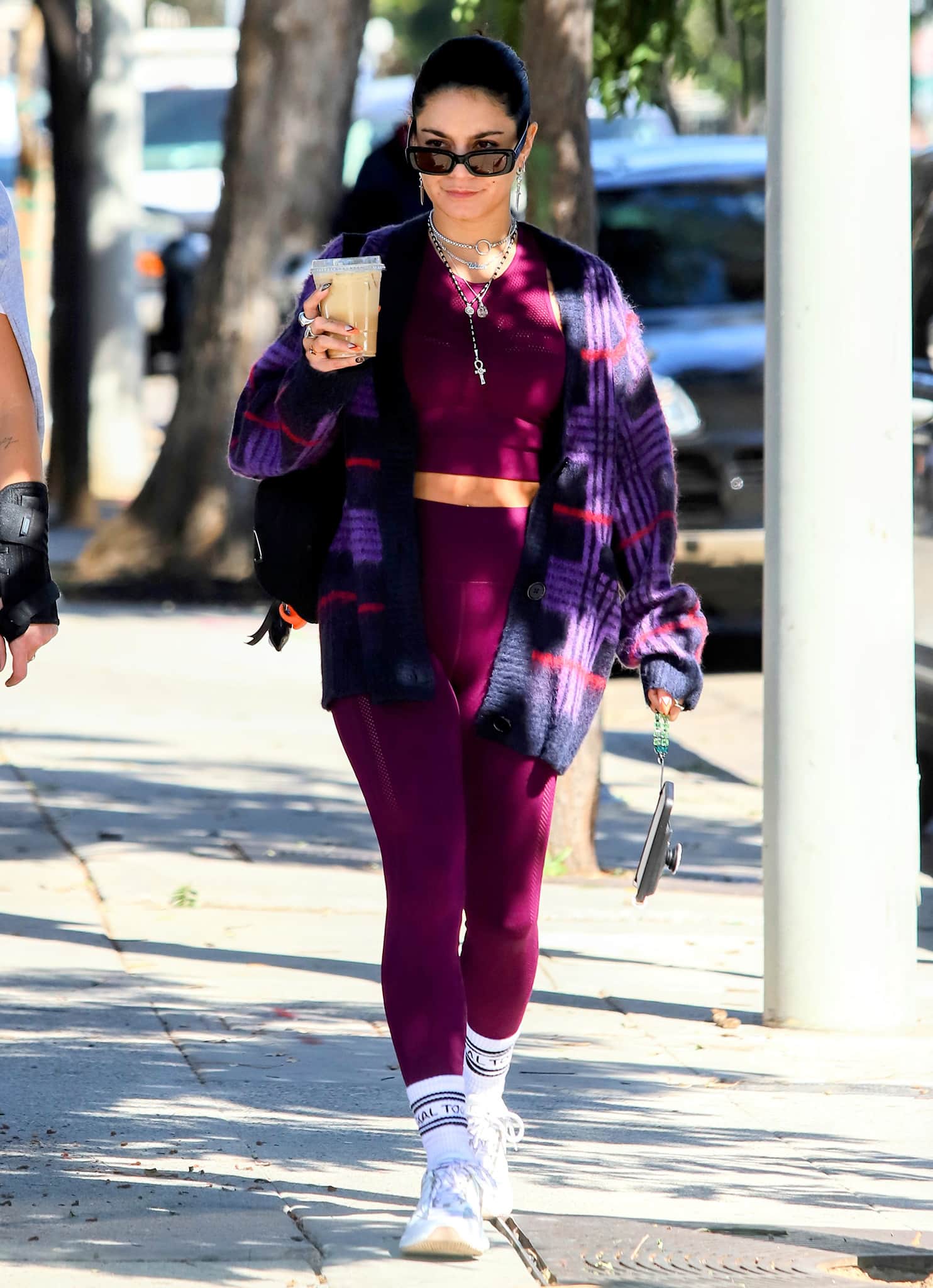Vanessa Hudgens keeps her post-gym look effortlessly cool, grounding a burgundy activewear set and fuzzy plaid cardigan with crisp white Mercer Amsterdam “Jupiter” sneakers, logo crew socks, and layered silver jewelry for a polished off-duty finish