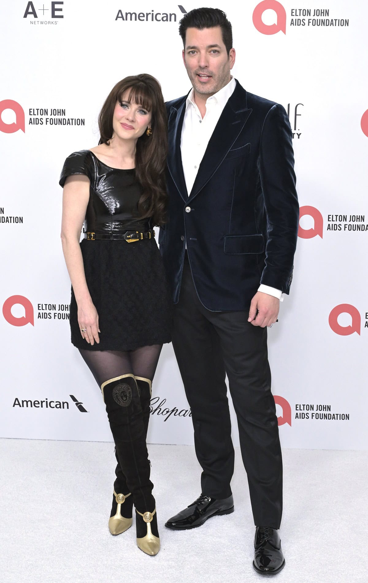 Zooey Deschanel looked petite next to Jonathan Scott as she rocked bold gold-trimmed Versace boots and a belted black mini at the Elton John Oscars party on March 2, 2025 in West Hollywood, California