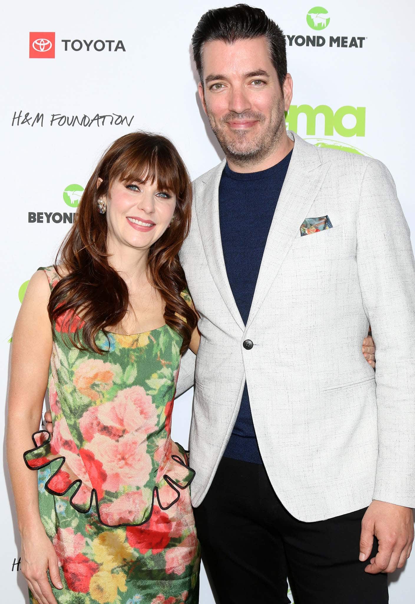 Zooey Deschanel embraced garden-party glam in a romantic floral dress with playful ruffle details, standing sweetly beside Jonathan Scott in a light linen blazer