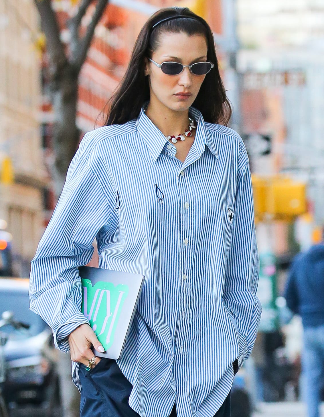 Slim sunglasses, a headband, statement jewelry, and a graphic laptop add personality to Bella Hadid’s menswear-inspired striped shirt