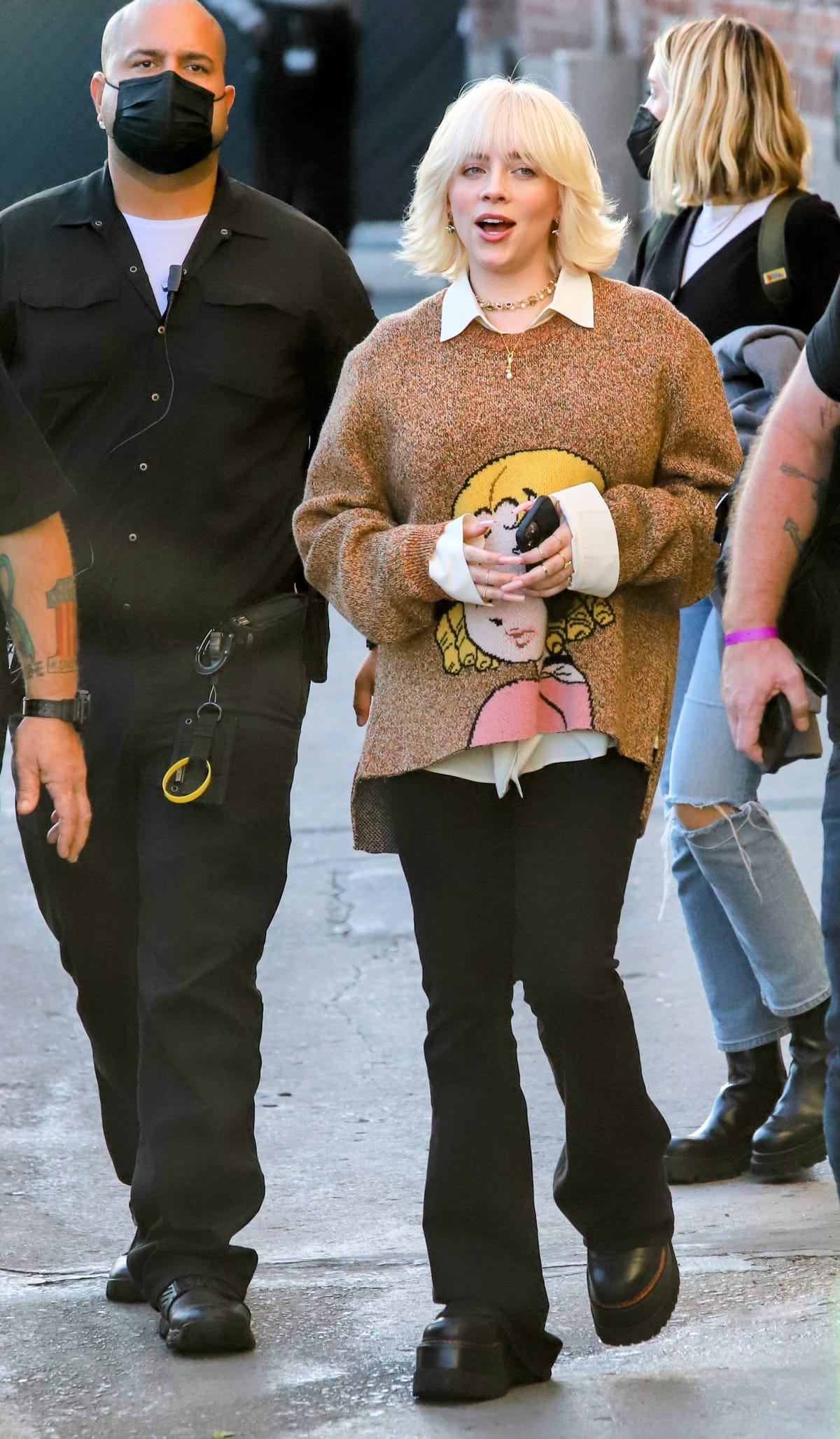 Billie Eilish steps out for a taping of Jimmy Kimmel Live! while promoting Happier Than Ever, pairing a playful oversized graphic sweater layered over a crisp collared shirt with black flared pants and towering Dr. Martens 2976 Max platform Chelsea boots that add height and edge to her relaxed, streetwear-inspired look
