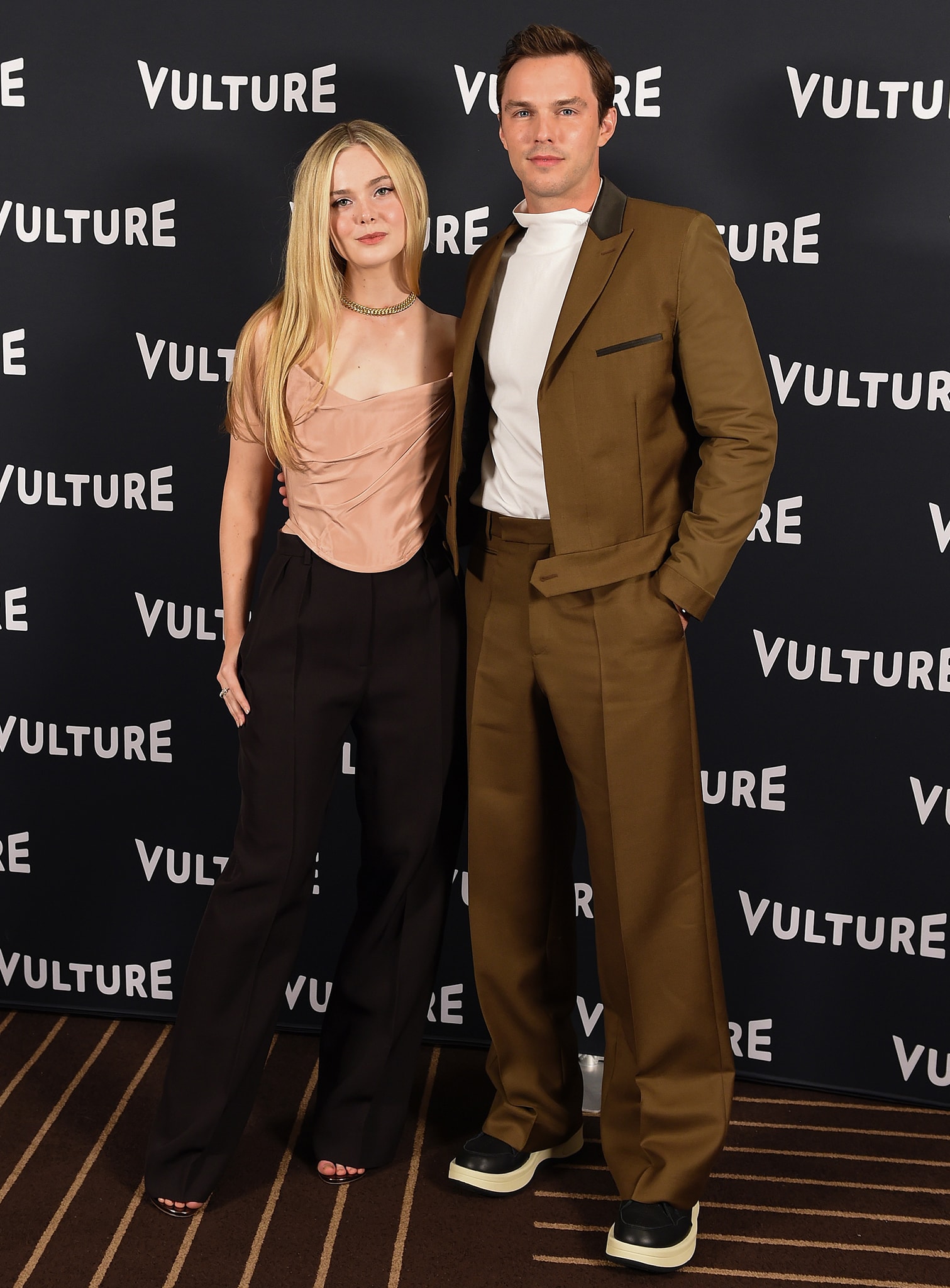 Elle Fanning and Nicholas Hoult pose at the Vulture Festival 2021, with Fanning pairing fluid black trousers and a blush satin corset top with sleek open-toe heels for a modern, pared-back red-carpet look