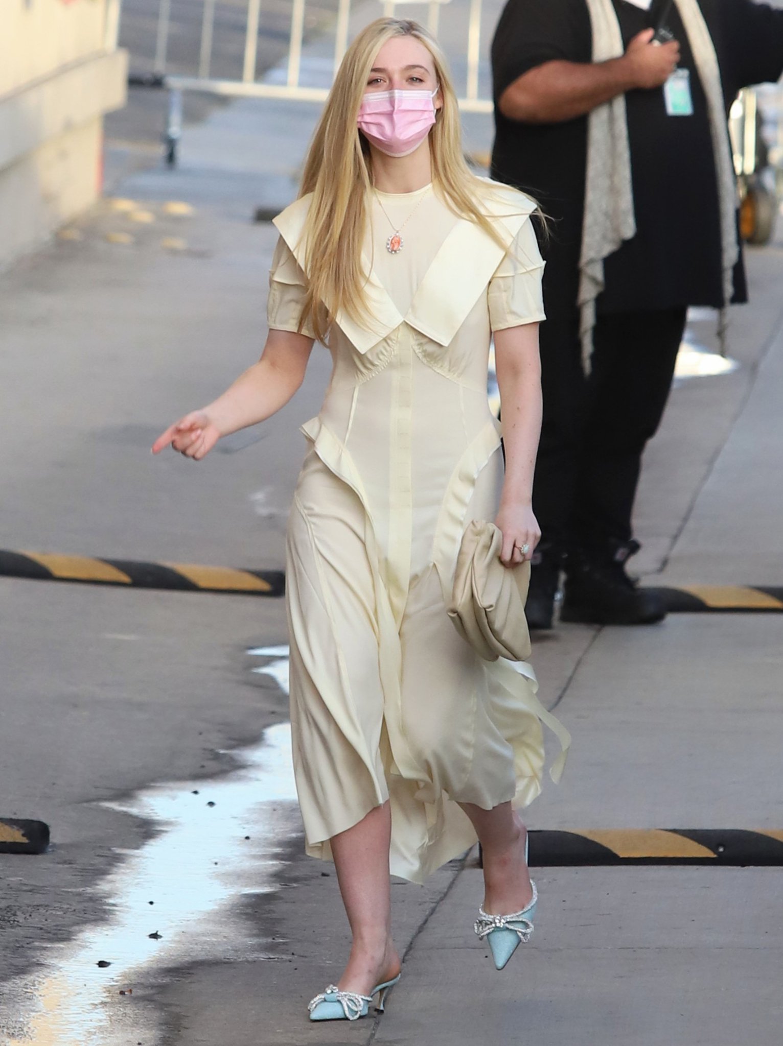 Elle Fanning heads to the Jimmy Kimmel Live studio in a softly structured pale-yellow midi dress, grounding the refined daytime look with glittering blue Mach Mach bow-embellished kitten-heel mules
