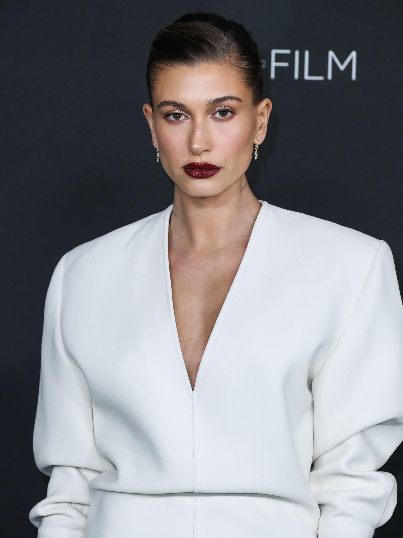 Hailey Bieber kept her beauty look minimal with softly glowing skin and dark berry lipstick that contrasted against the crisp white gown