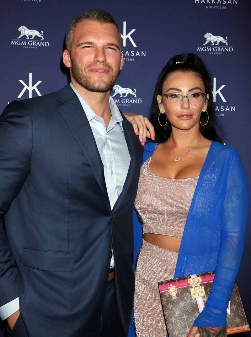JWoww glows in a shimmering pink crop top and matching skirt, accessorized with a blue sheer cover-up and chic glasses, while standing alongside Zack Carpinello, who looks sharp in a tailored navy suit, at an event at Hakkasan Nightclub