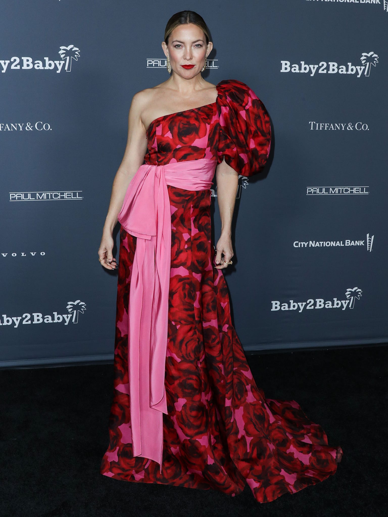 Kate Hudson stuns in a red floral Carolina Herrera Resort 2022 one-shoulder gown, its sweeping hem skimming the floor and discreetly concealing her heels