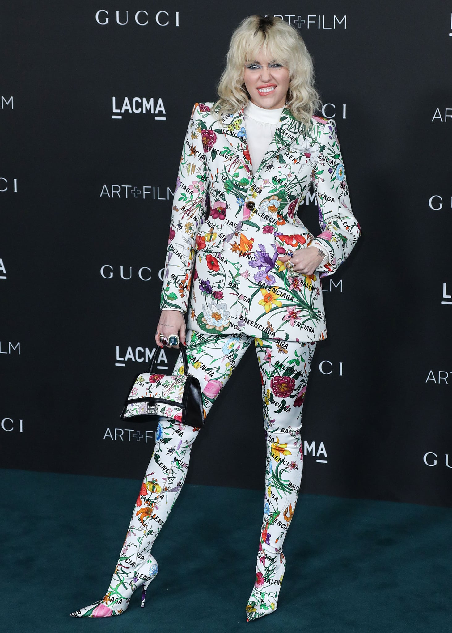 Miley Cyrus showcases the Gucci x Balenciaga Hacker Project's signature pantashoes, with the floral print extending seamlessly from her tailored trousers into sharply pointed stiletto boots