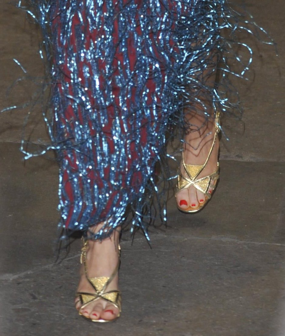 Miley Cyrus showcases her metallic gold Gucci sandals beneath the shimmering fringe hem of her Love Parade gown, pairing the strappy heels with bright red pedicure polish for a touch of vintage-inspired glamour