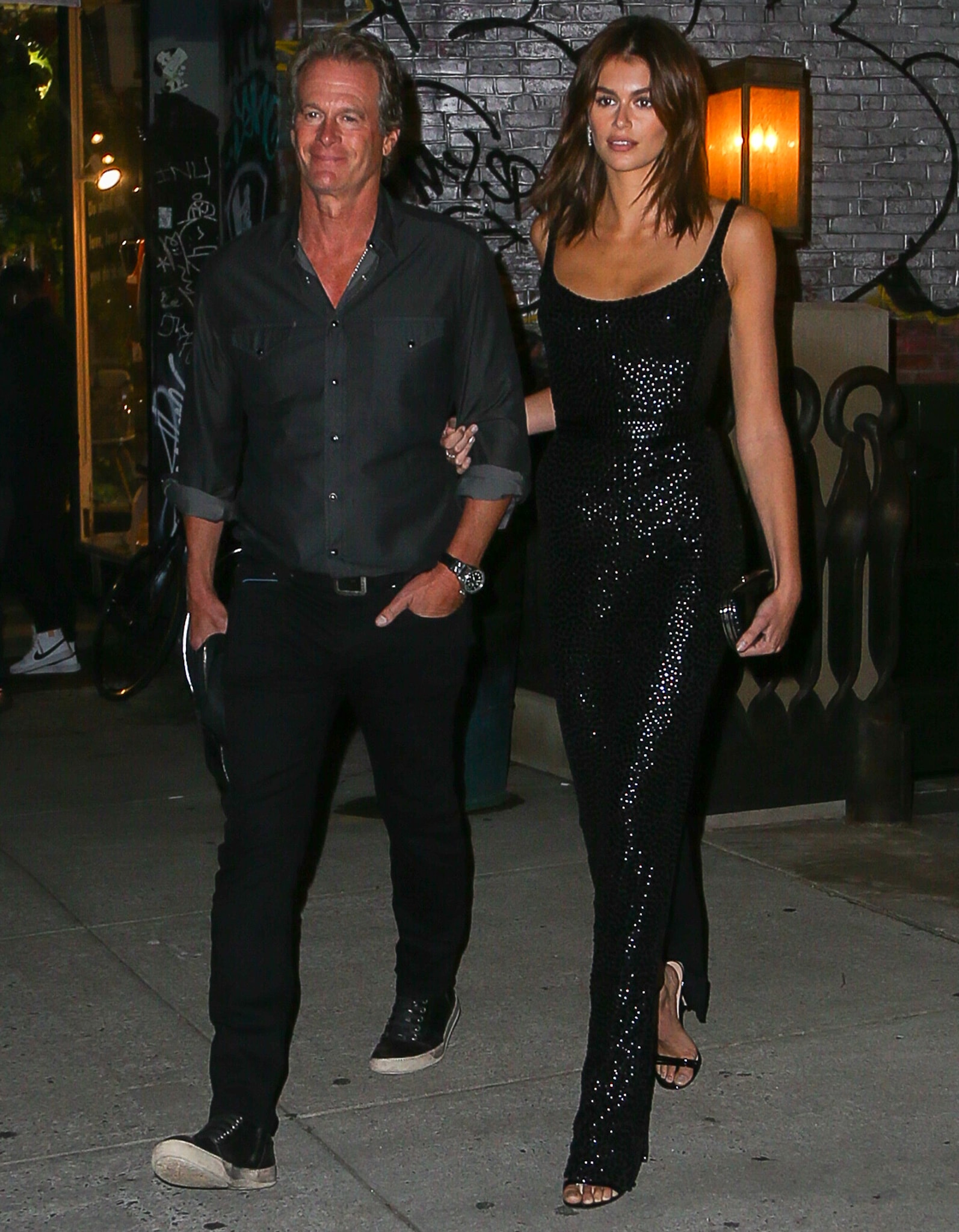 Rande Gerber and Kaia Gerber step out for dinner in New York City ahead of the DKMS gala, with Kaia continuing the look in her shimmering black Marc Jacobs gown, paired with minimalist black strappy sandals that keep the silhouette sleek from shoulder to toe