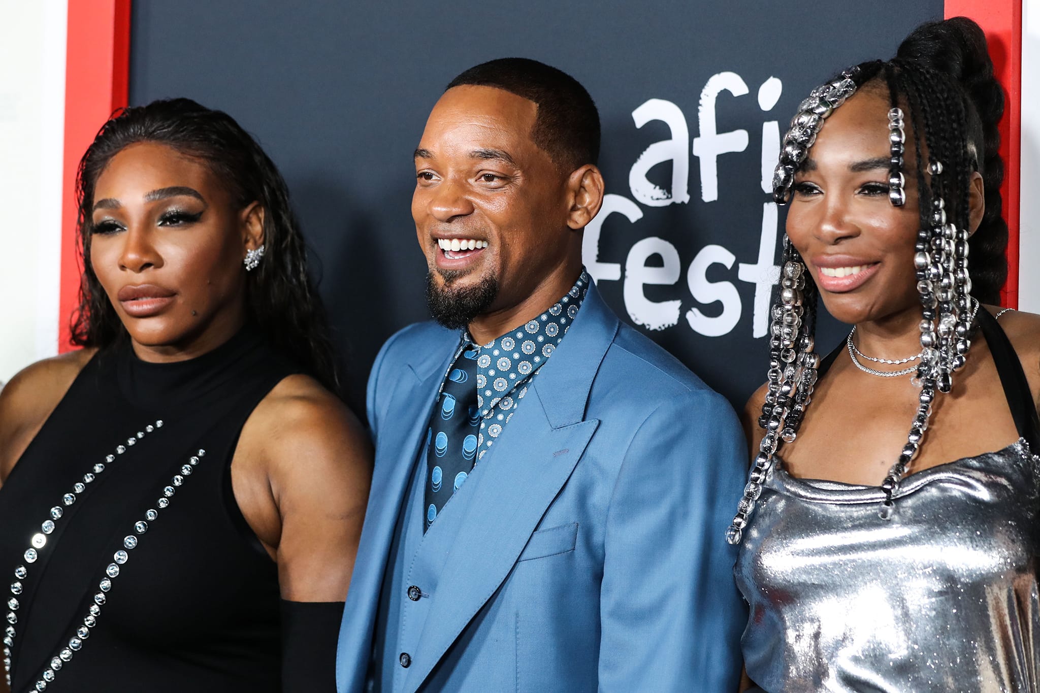 Serena Williams stuns in a sleek black embellished ensemble, while Venus Williams sparkles in a silver velvet Bach Mai gown, as they pose alongside Will Smith, who stars as Richard Williams in King Richard, a biopic celebrating the sisters' father and coach