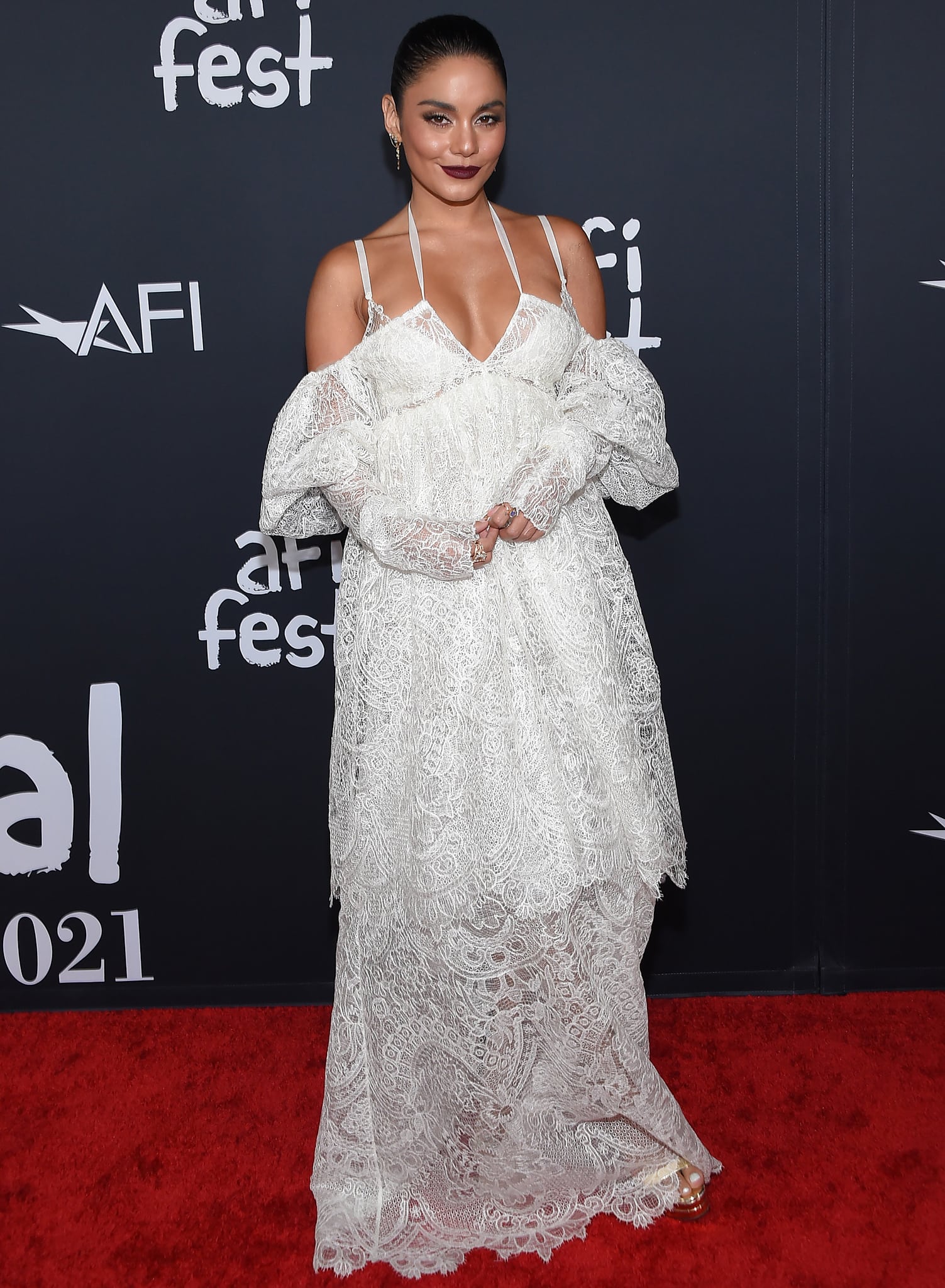 Vanessa Hudgens’ plunging, lingerie-inspired Vera Wang gown cascades in airy, tiered lace, subtly revealing a glimpse of her towering Versace platform heels—gold-toned and glossy—peeking out beneath the hem, adding height and a modern edge to the otherwise ethereal silhouette