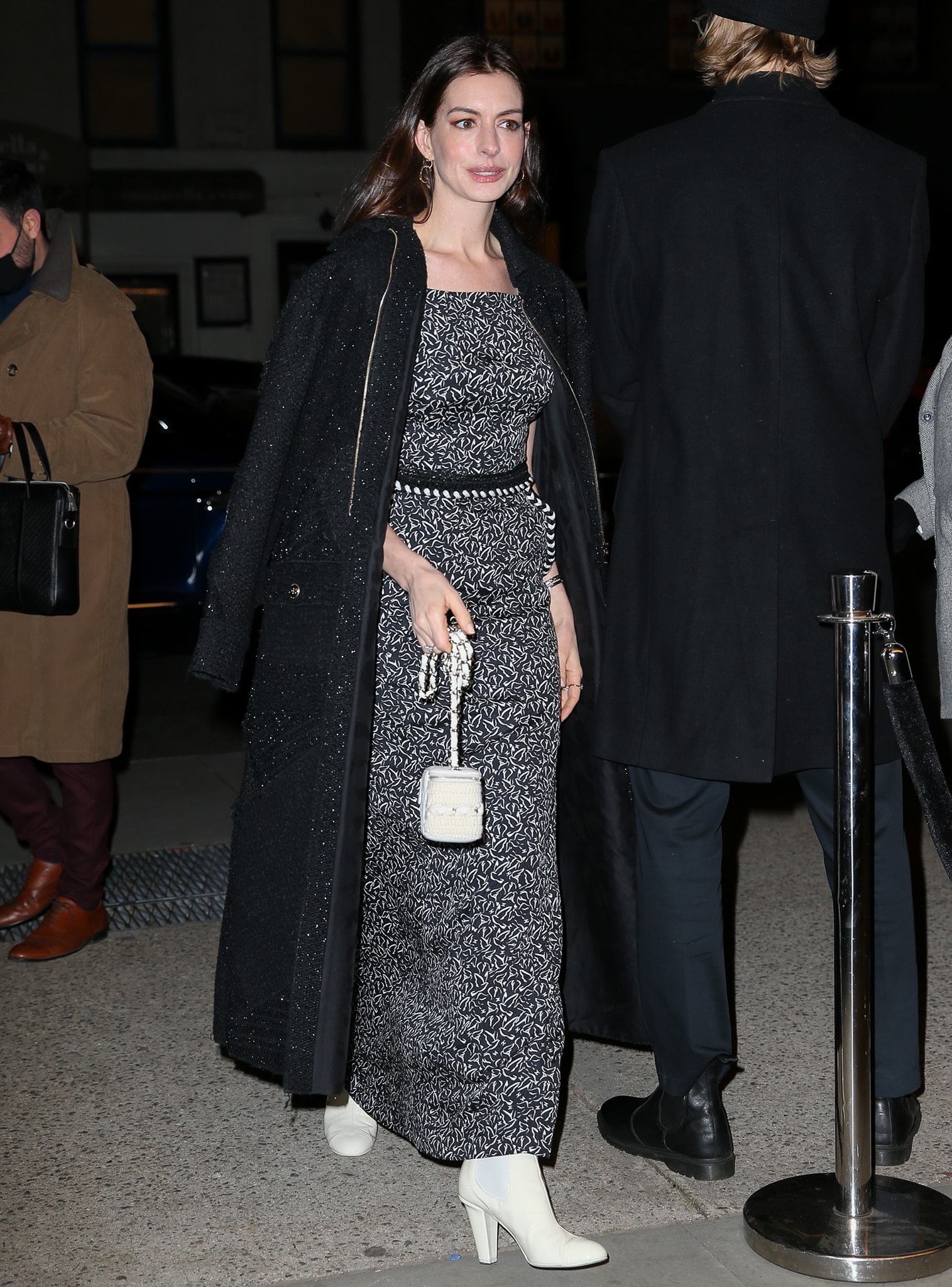 Anne Hathaway layers her dove-print Chanel gown with a textured black tweed coat and finishes the look with white Chanel ankle boots