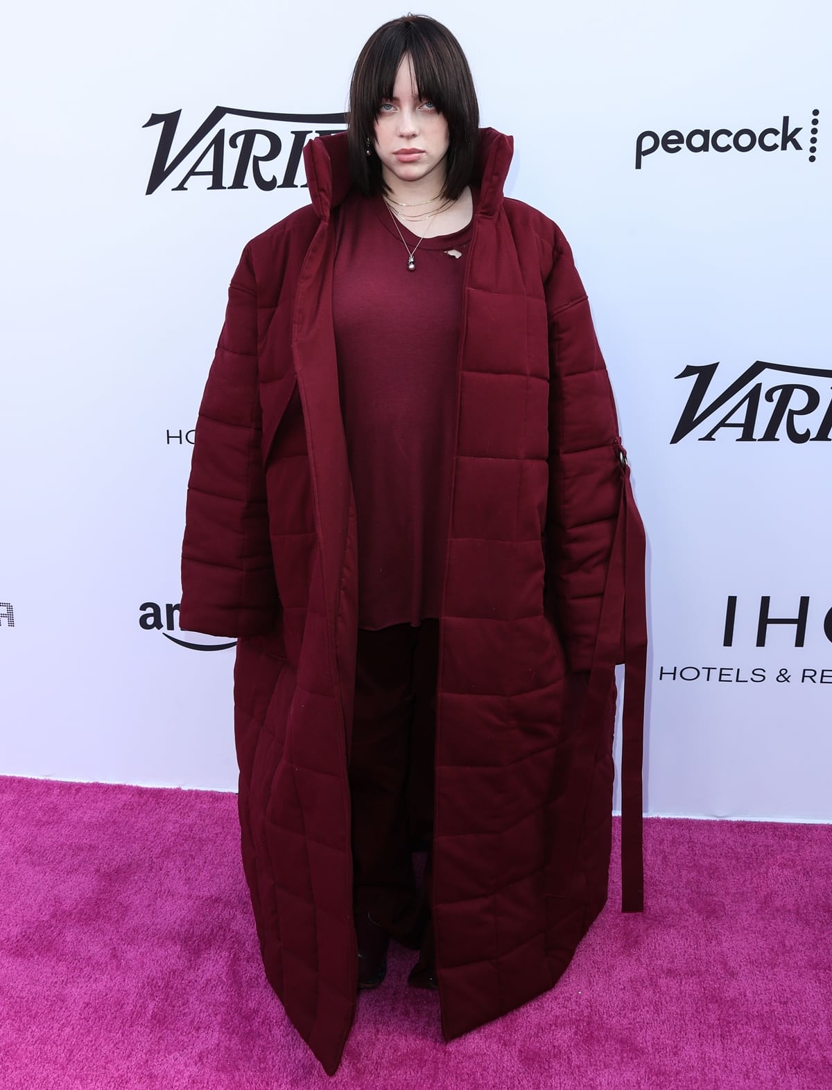 Billie Eilish made a bold statement at Variety’s 2021 Hitmakers Brunch in a head-to-toe burgundy ensemble styled by Amanda Merten, featuring an oversized quilted coat, matching layers, and Raf Simons AW14 Sterling Ruby Bunny Boots from Artifact NY